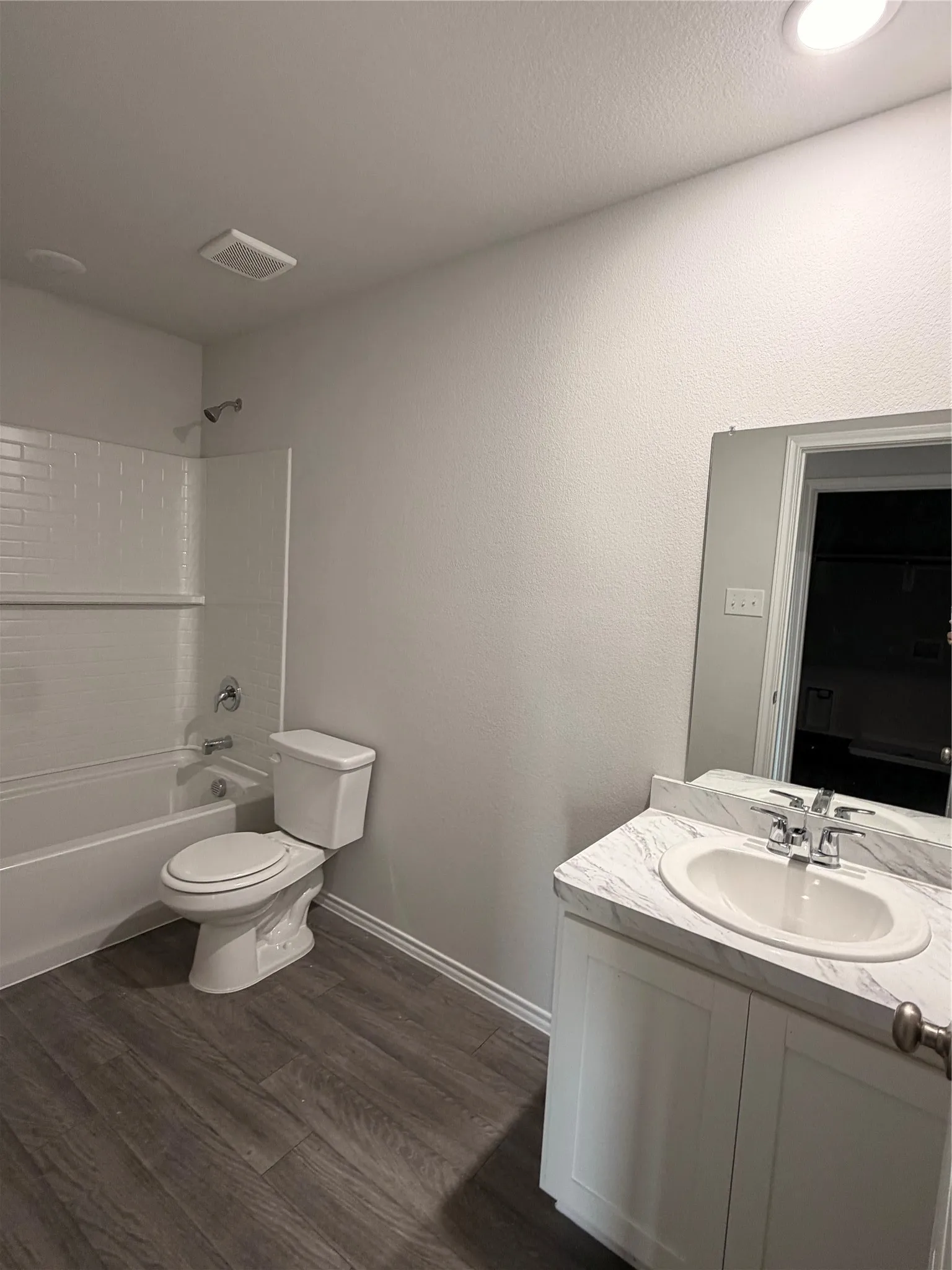 Bathroom featuring a white bathtub with subway tile surround, wood-finish flooring, white vanity with integrated sink, and a framed mirror