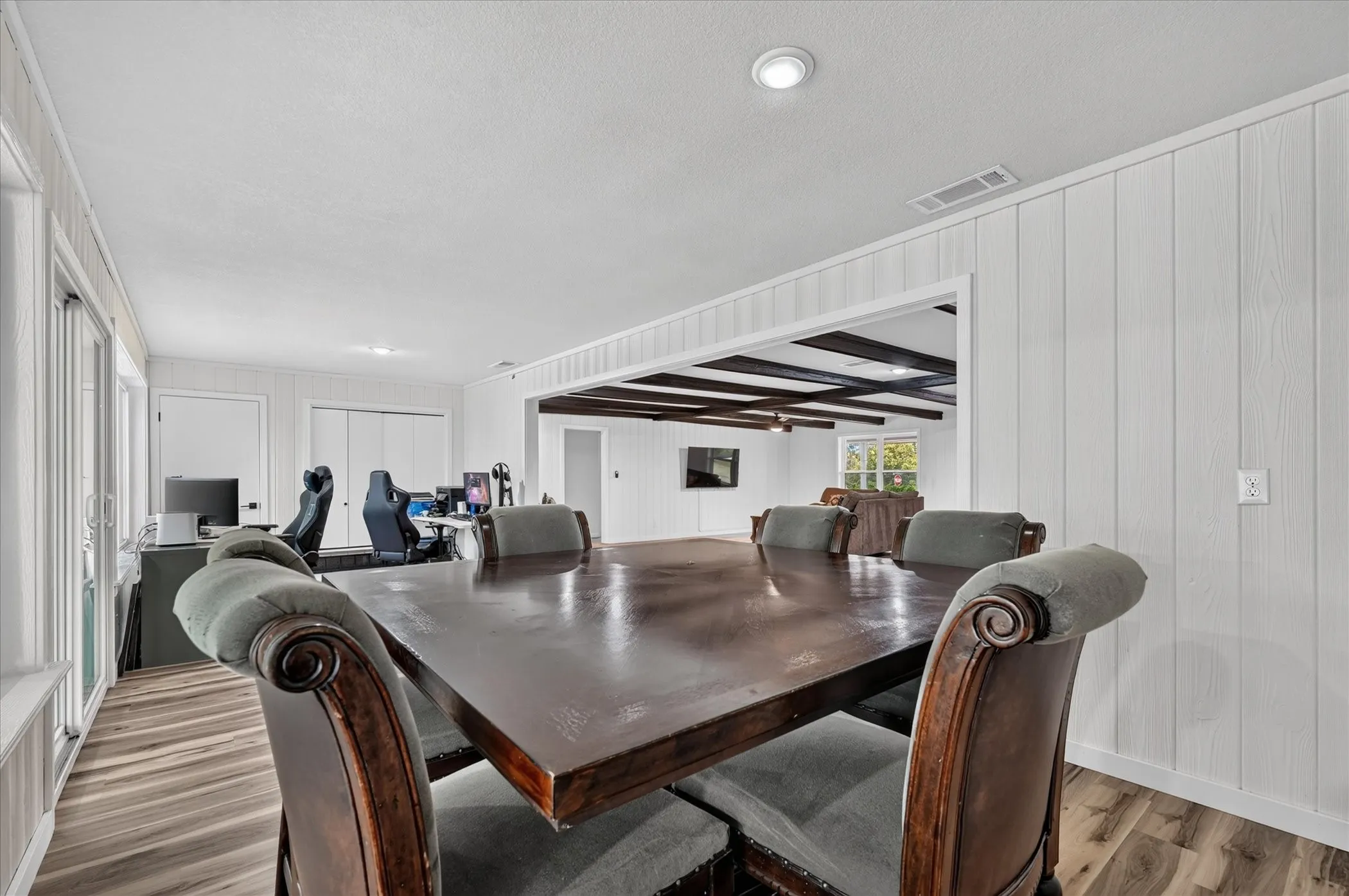 Wood-finish flooring throughout, white vertical plank wall panels, and an open doorway reveal dark wood-beamed ceilings