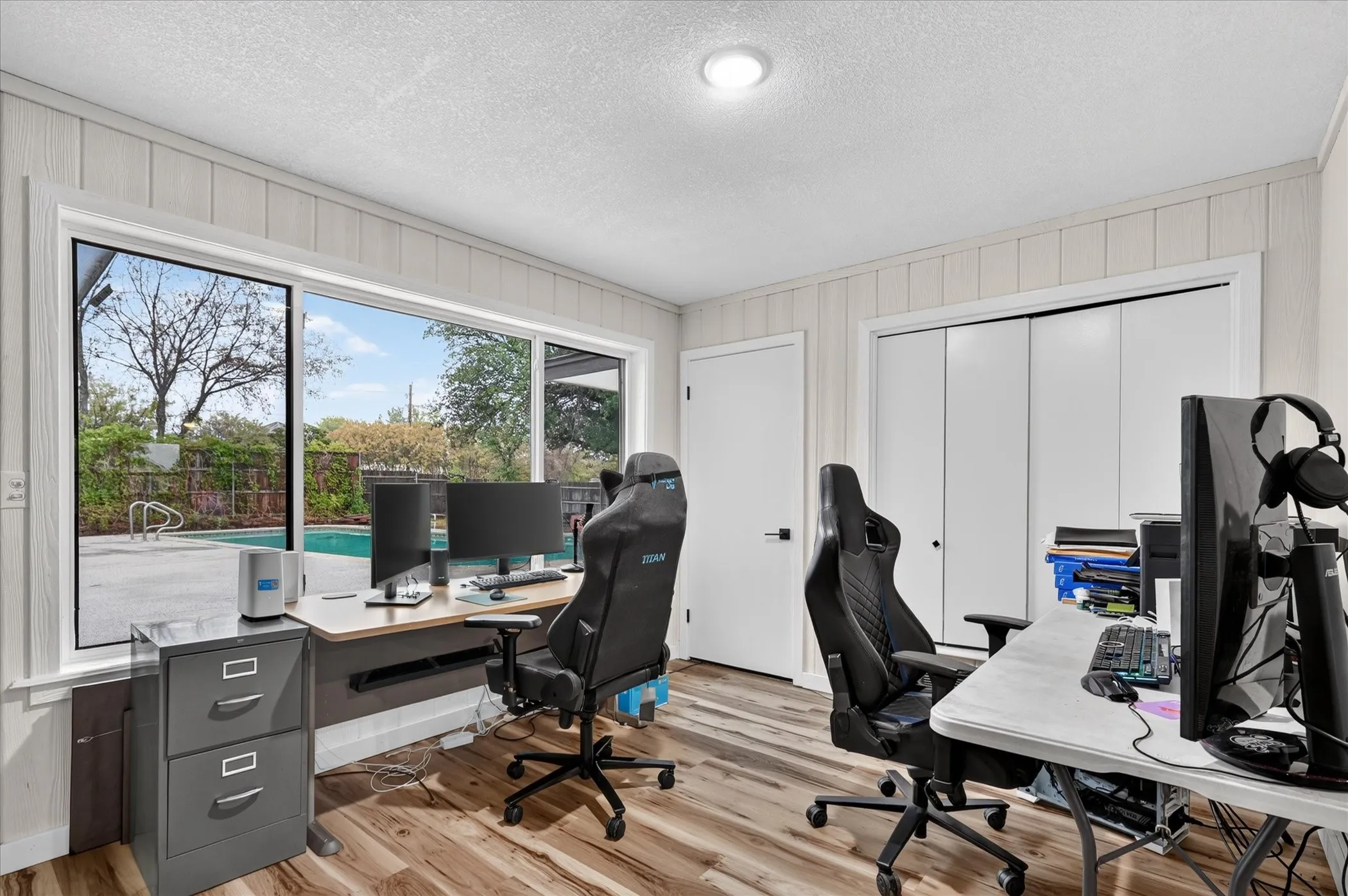Wide window overlooking a swimming pool, wood-finish flooring, white panel walls, recessed lighting, and white bi-fold closet doors