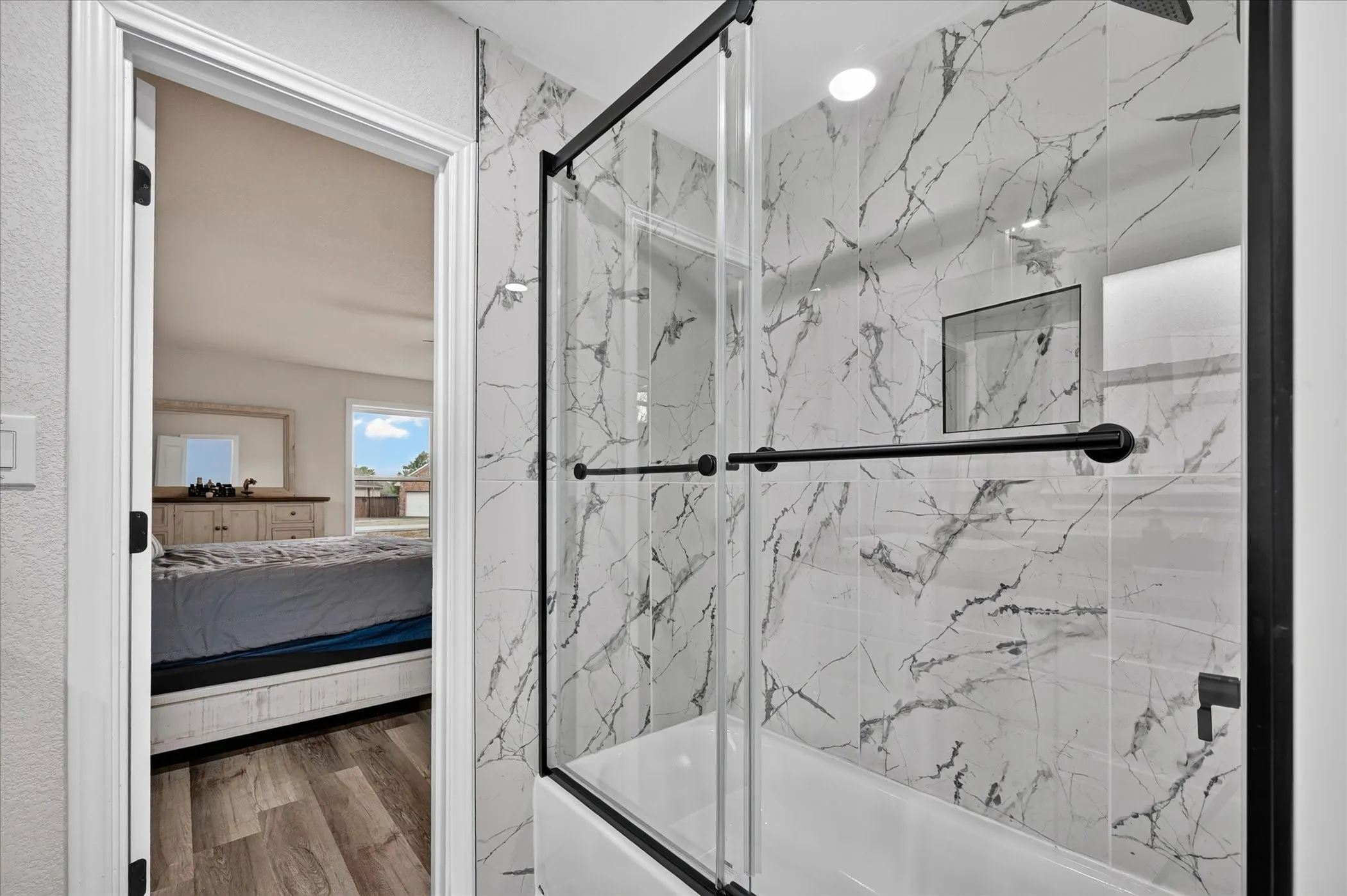 Tub and shower combination with a black-framed glass enclosure, white tile surround with gray veining, and a recessed shower niche