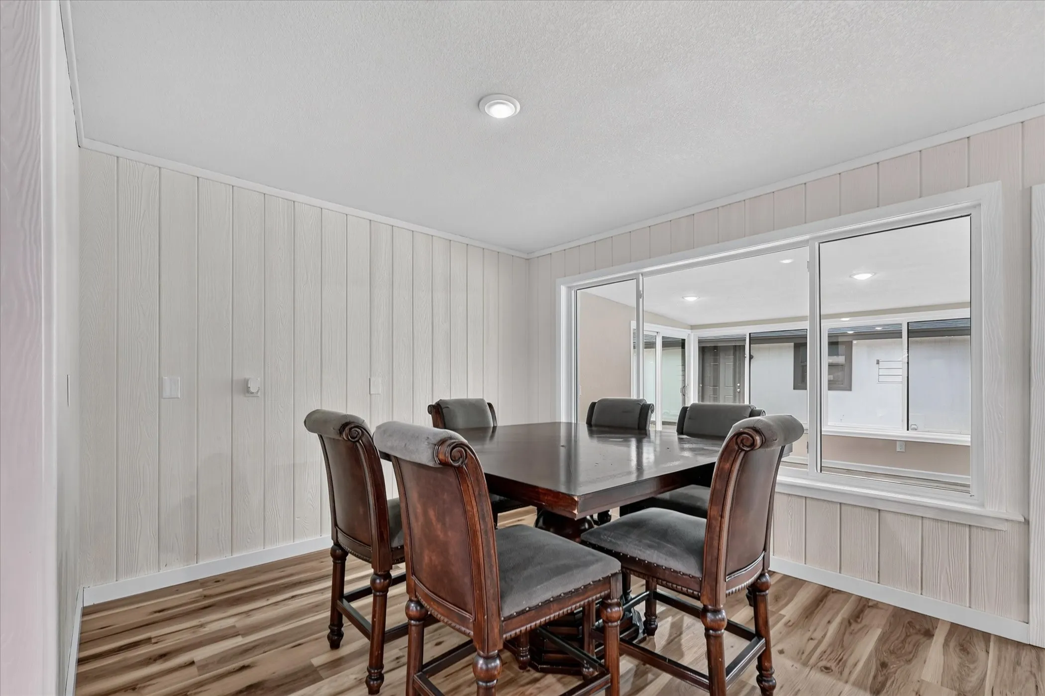 Wood-finish flooring with white paneled walls, recessed ceiling lighting, and a large multi-pane window