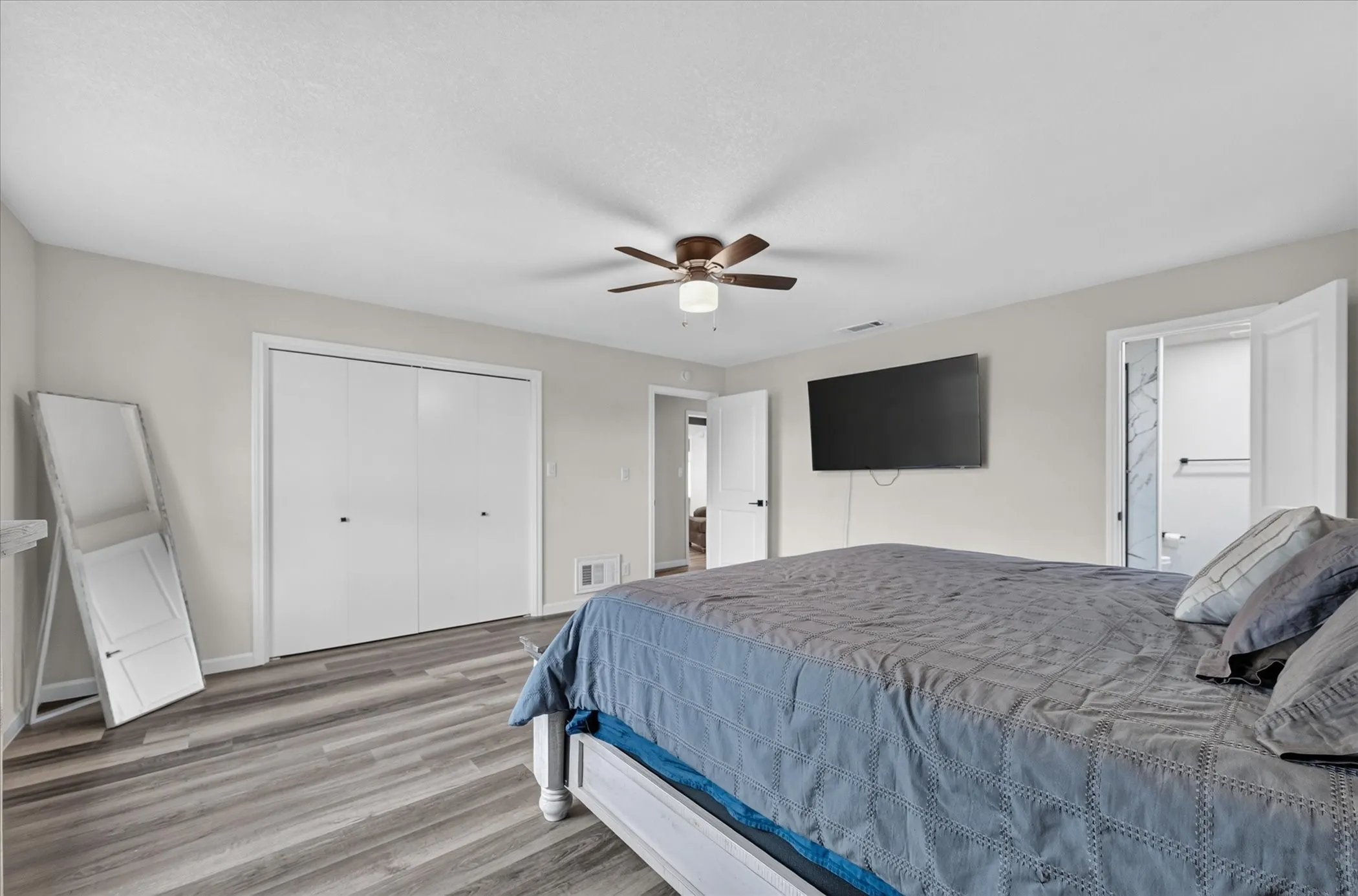 Wood-finish flooring, ceiling fan with integrated lighting, double-door closet, and an open doorway to another room