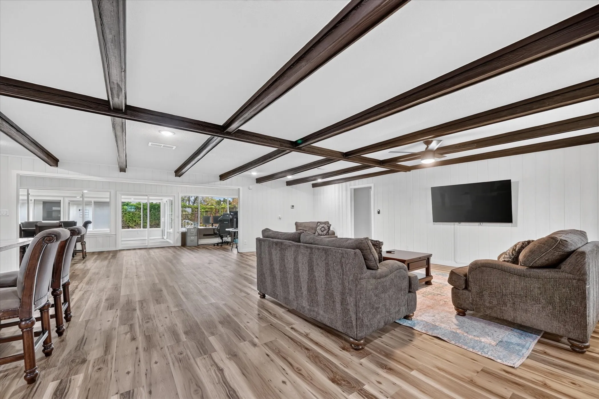 Spacious living area featuring wood-finish flooring, white paneling, and a beamed ceiling