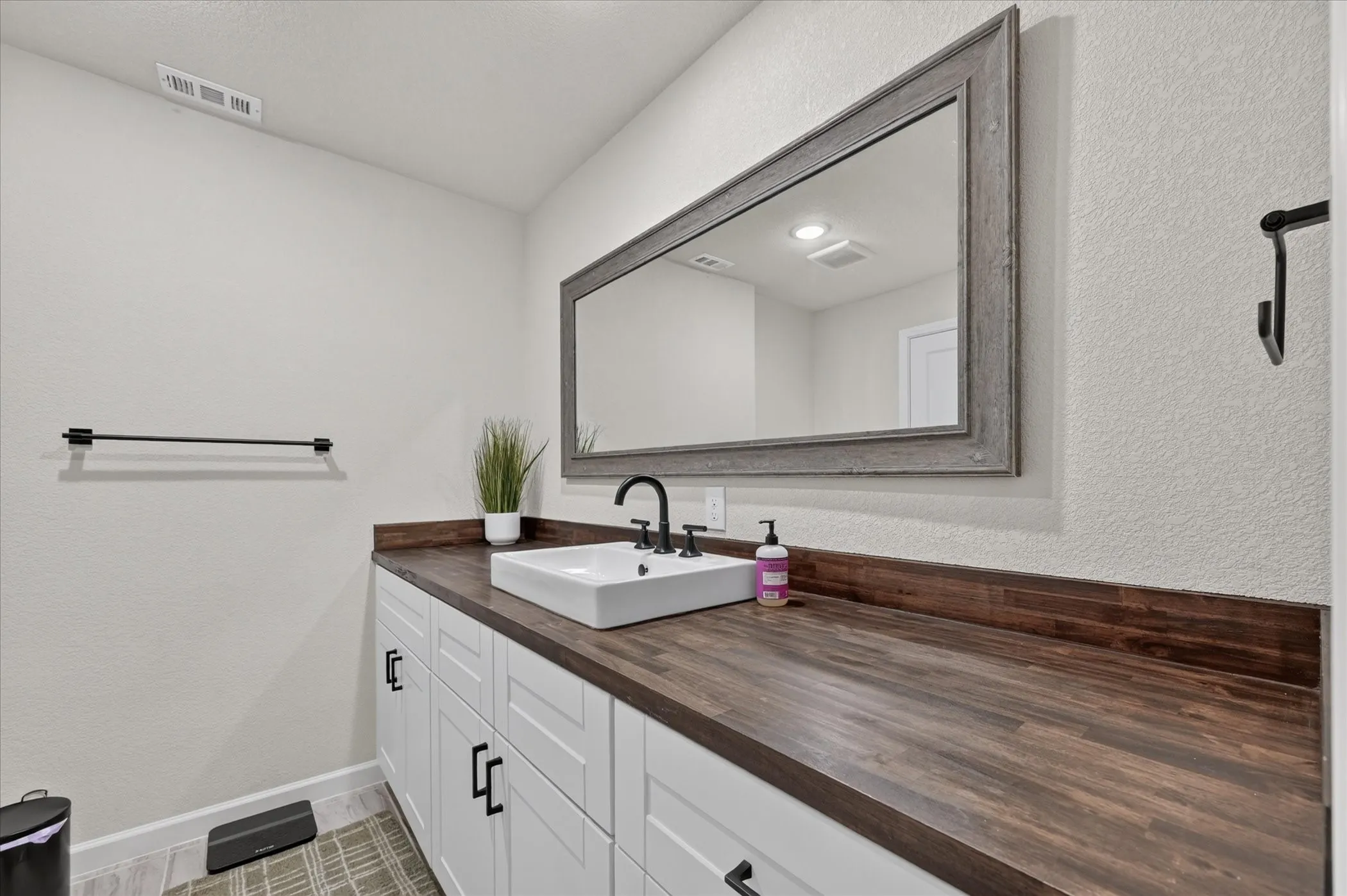 Vanity featuring a rectangular vessel sink, dark wood-finish countertop, white cabinetry with black hardware, and a large framed mirror