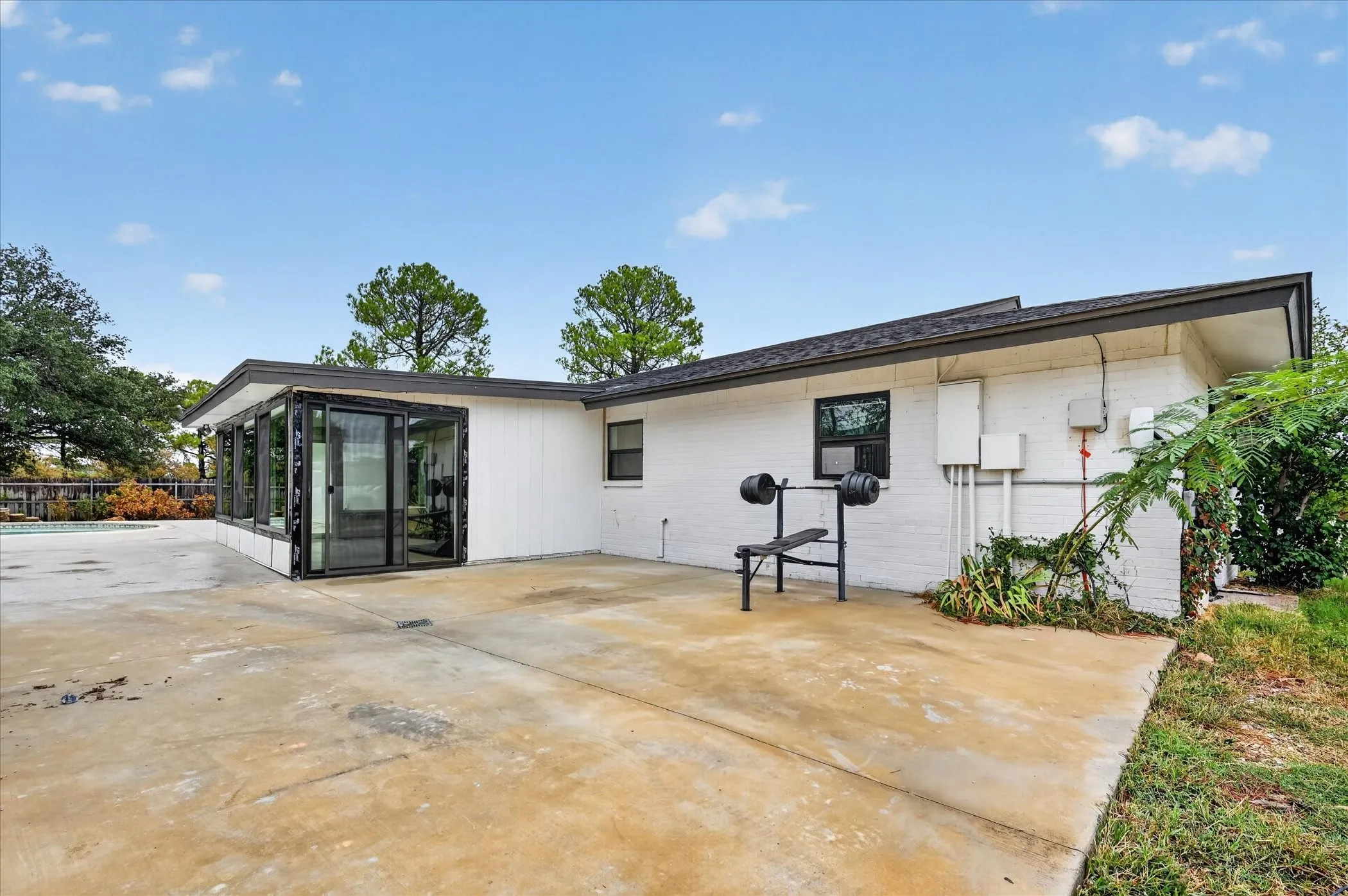 White brick exterior with dark trim, featuring a sunroom with black-framed windows and a flat roofline