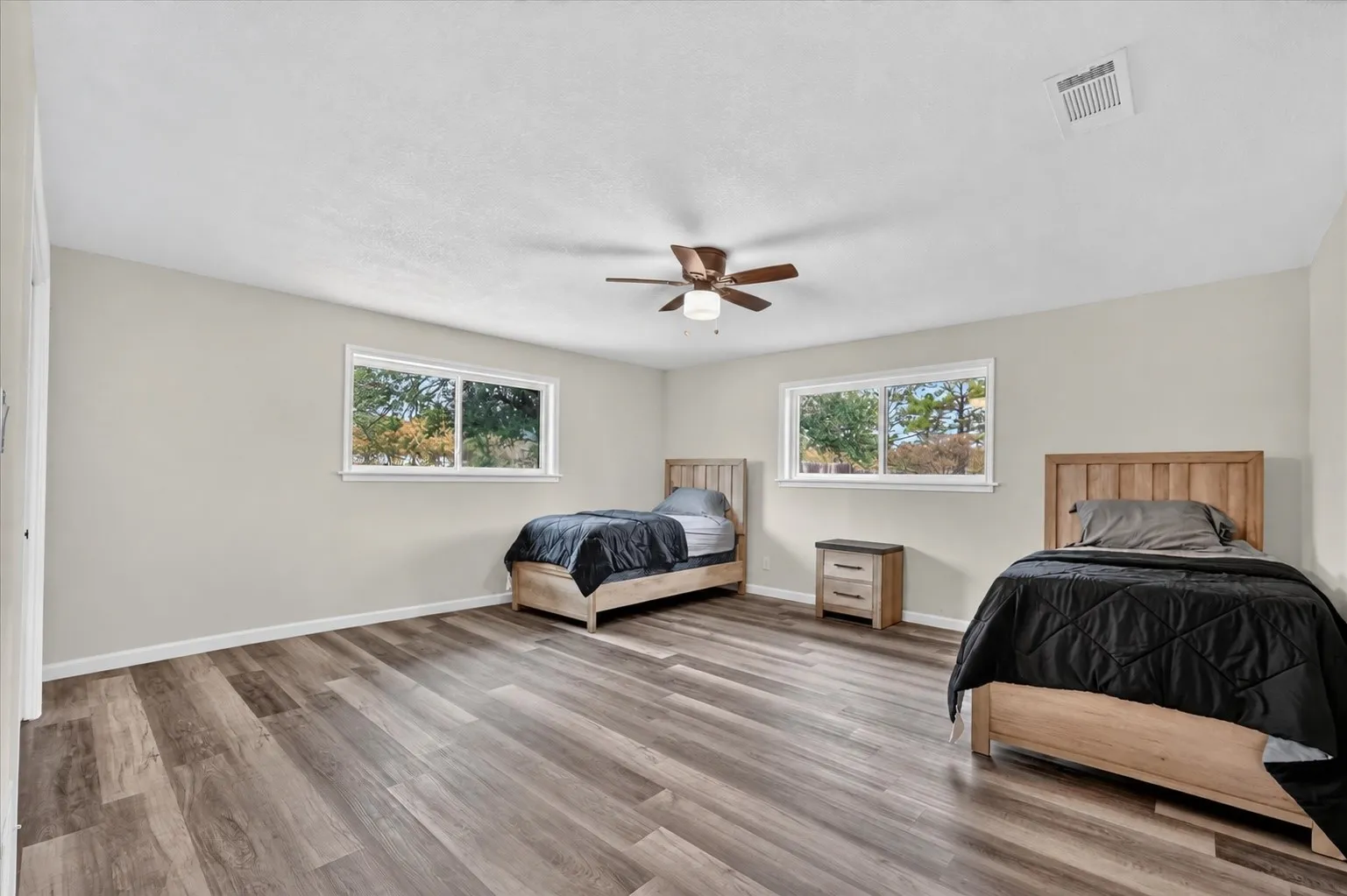 Wood-finish flooring throughout, two large windows, a ceiling fan with integrated lighting, and neutral wall paint