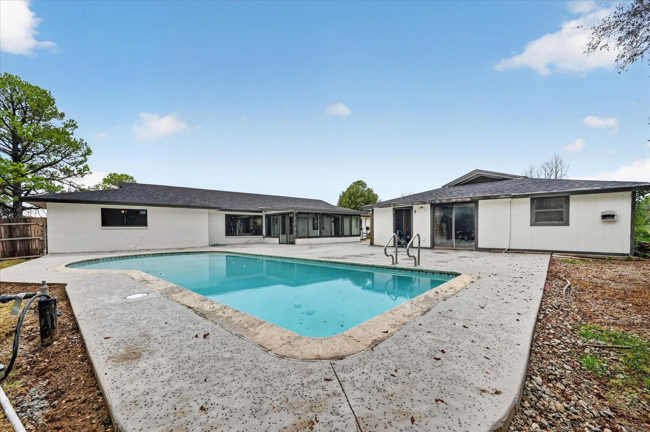 Outdoor swimming pool with concrete decking, surrounded by white-painted exterior walls, dark-framed windows, and dark shingle roofing