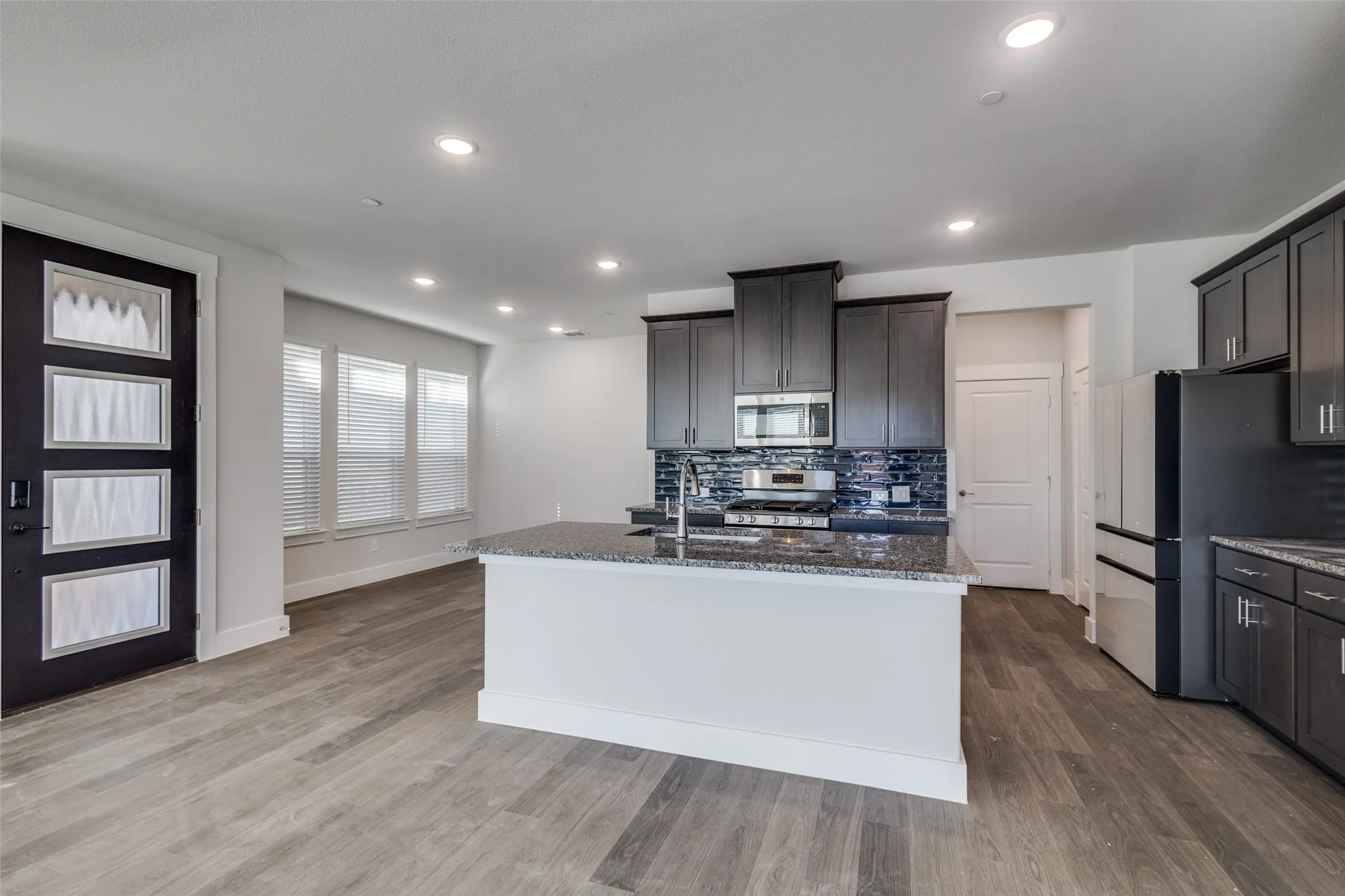 Kitchen featuring dark stone countertops, wood-type flooring, an island with sink, and appliances with stainless steel finishes