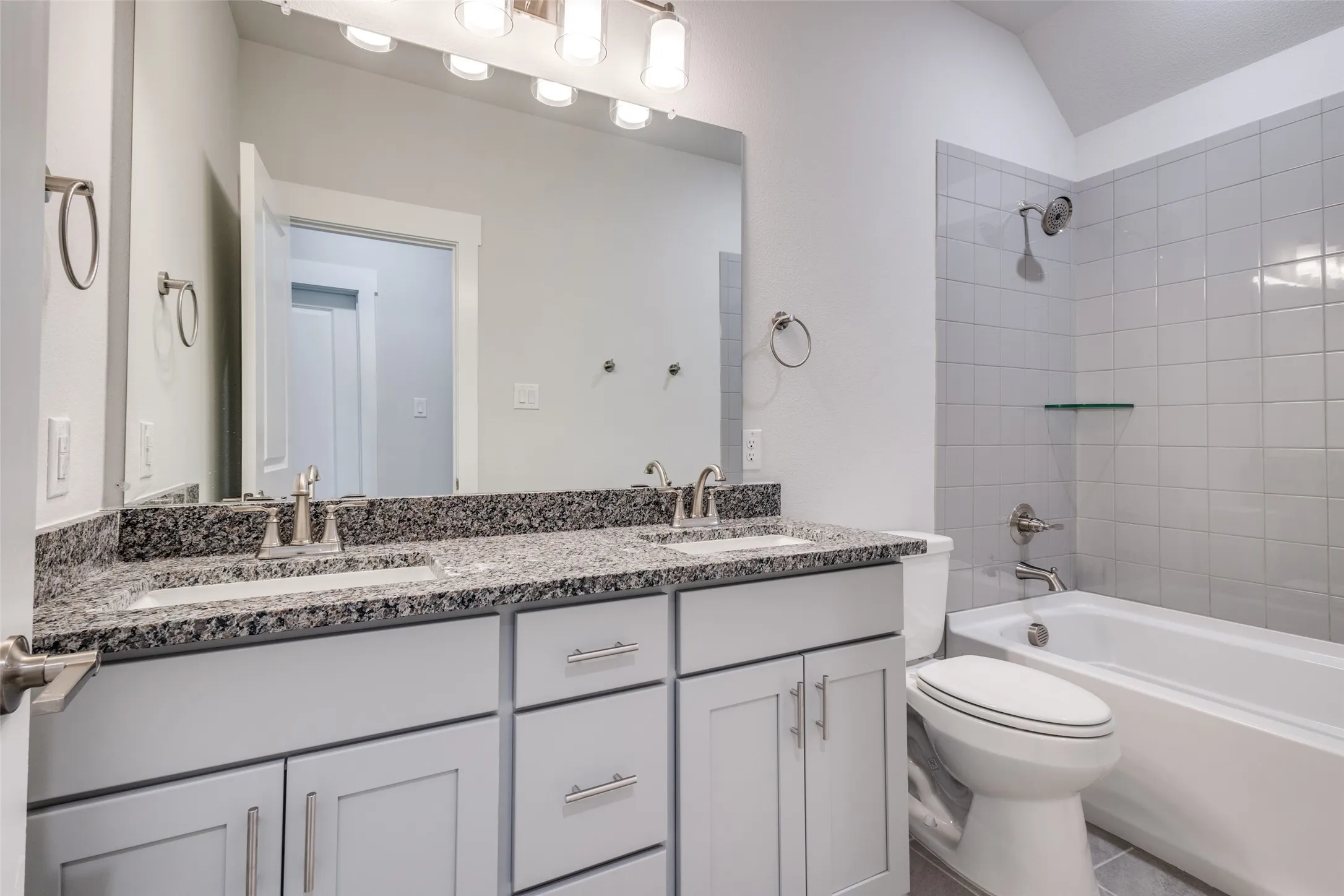 Full bathroom with vanity, tiled shower / bath, vaulted ceiling, tile patterned flooring, and toilet