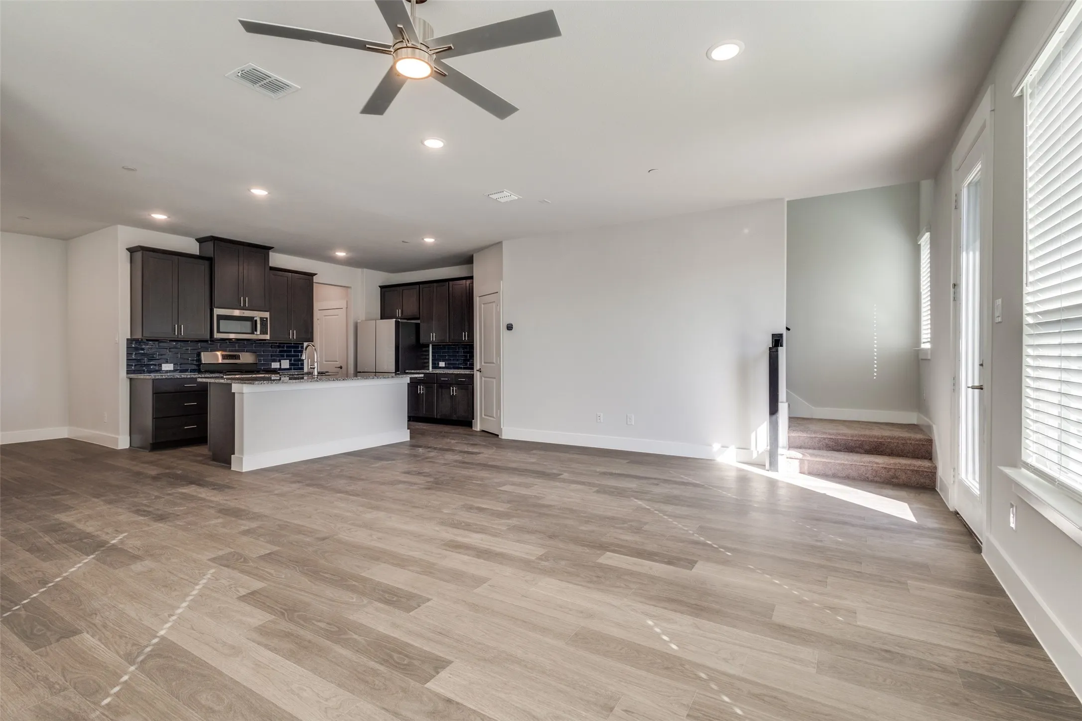 Kitchen with ceiling fan, stainless steel appliances, tasteful backsplash, light hardwood / wood-style flooring, and a center island with sink