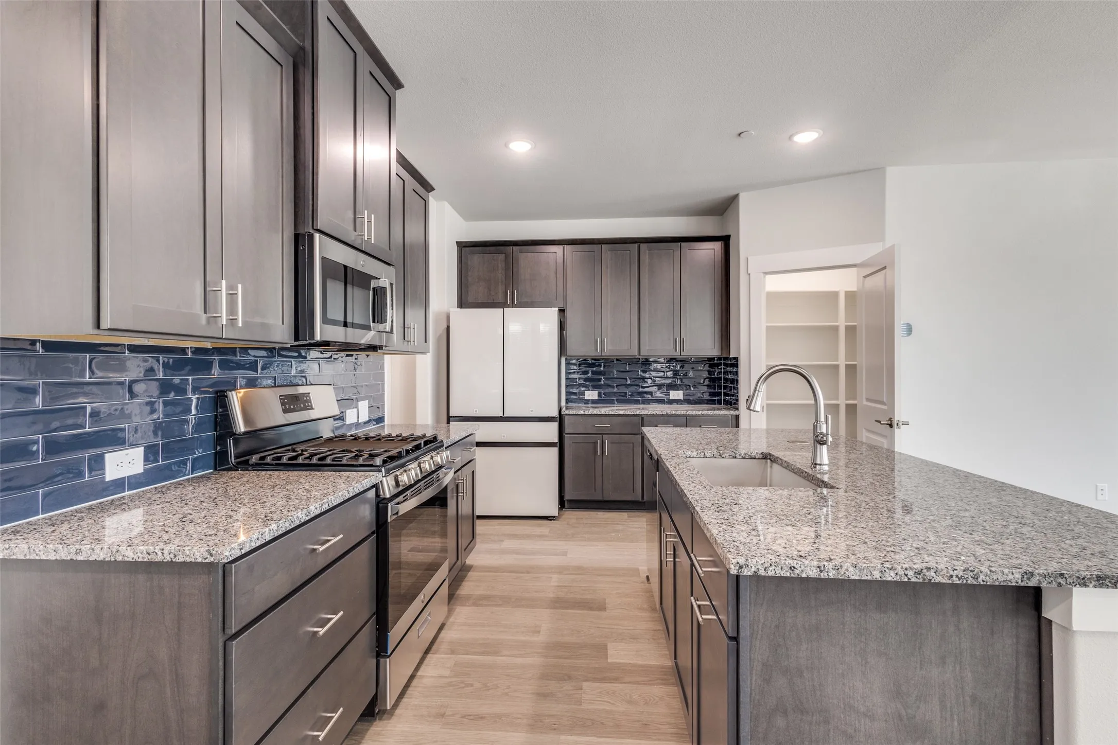 Kitchen with sink, tasteful backsplash, a center island with sink, appliances with stainless steel finishes, and light wood-type flooring