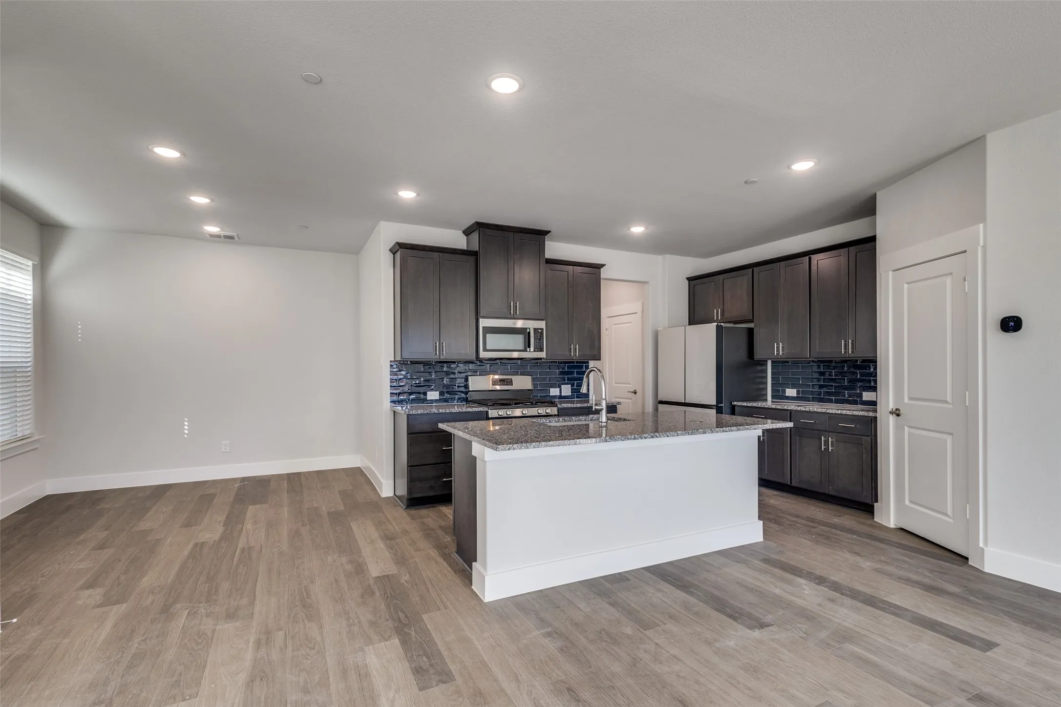 Kitchen featuring dark brown cabinetry, decorative backsplash, a center island with sink, appliances with stainless steel finishes, and light wood-type flooring