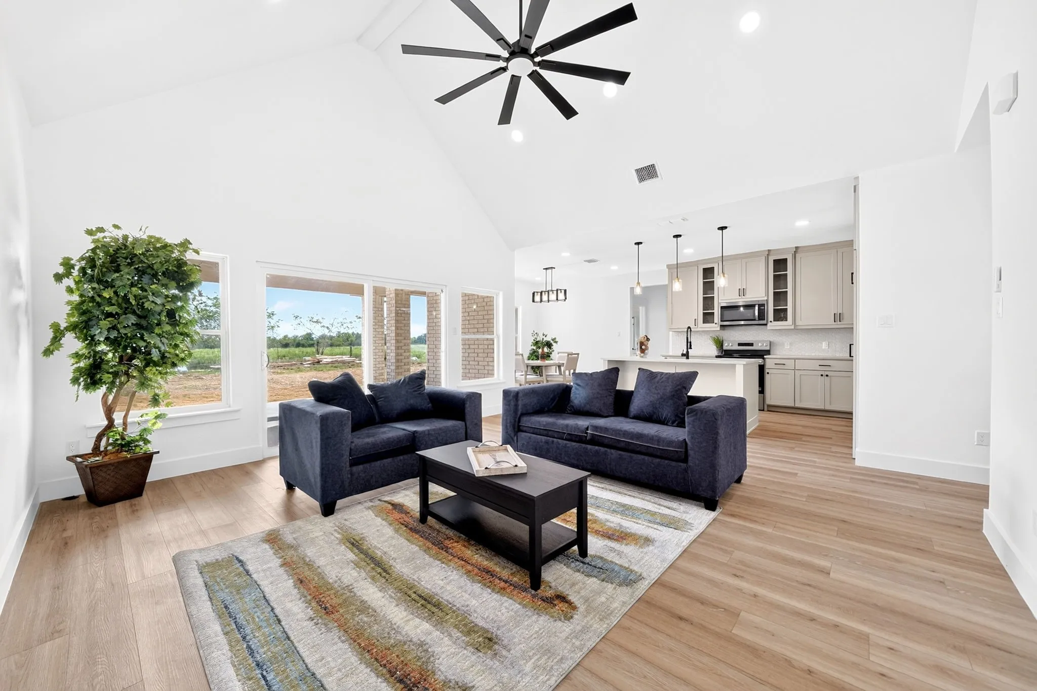 Vaulted ceiling with a contemporary ceiling fan, wood-finish flooring, ample natural light, and a kitchen featuring a central island and pendant lighting