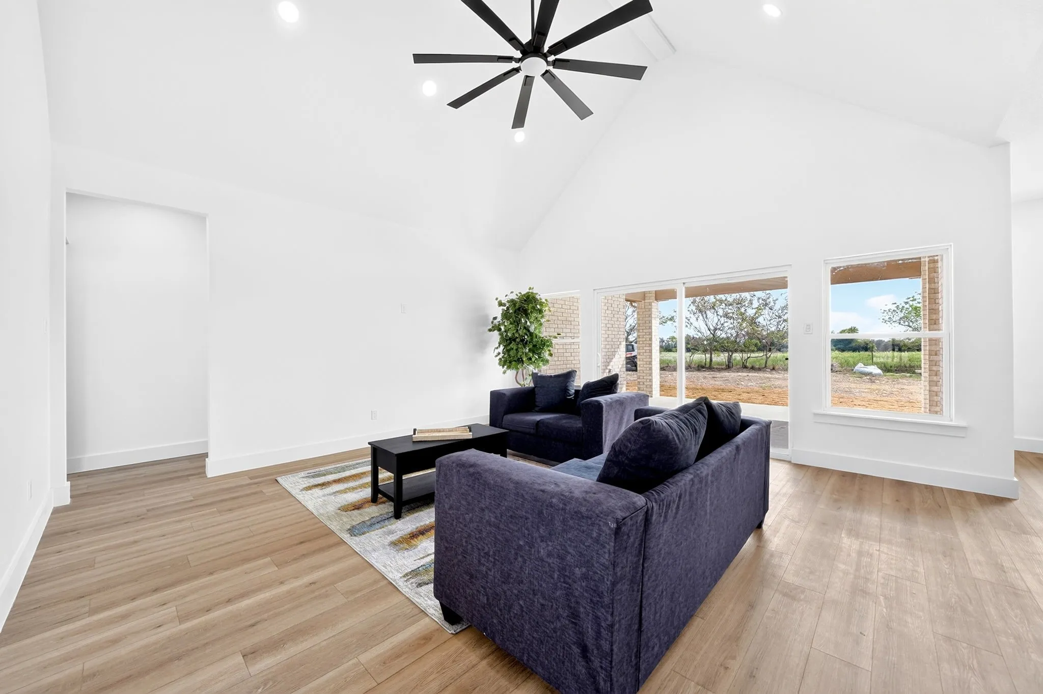 Vaulted ceiling with recessed lighting, wood-finish flooring, sliding glass patio doors, and a large window
