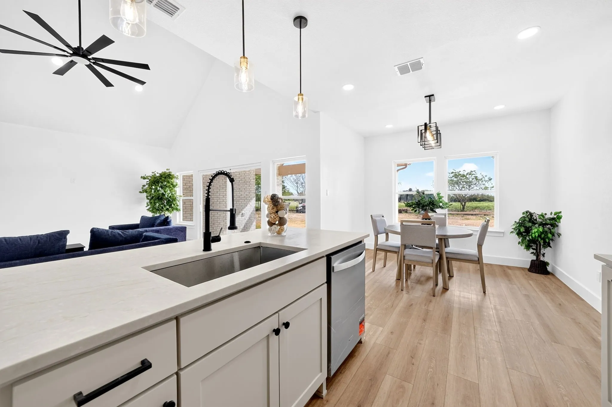Kitchen island with a stainless steel sink and matte black faucet, open-concept layout, vaulted ceiling, recessed lighting, and wood-finish flooring