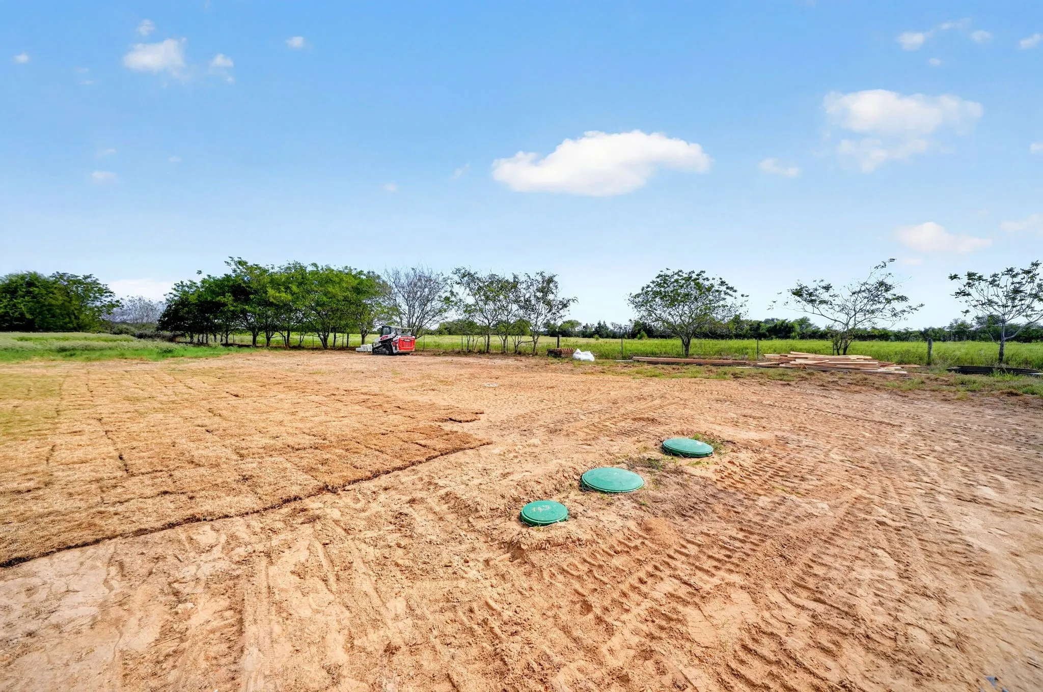 Expansive land with partial sod installation and mature trees along the perimeter