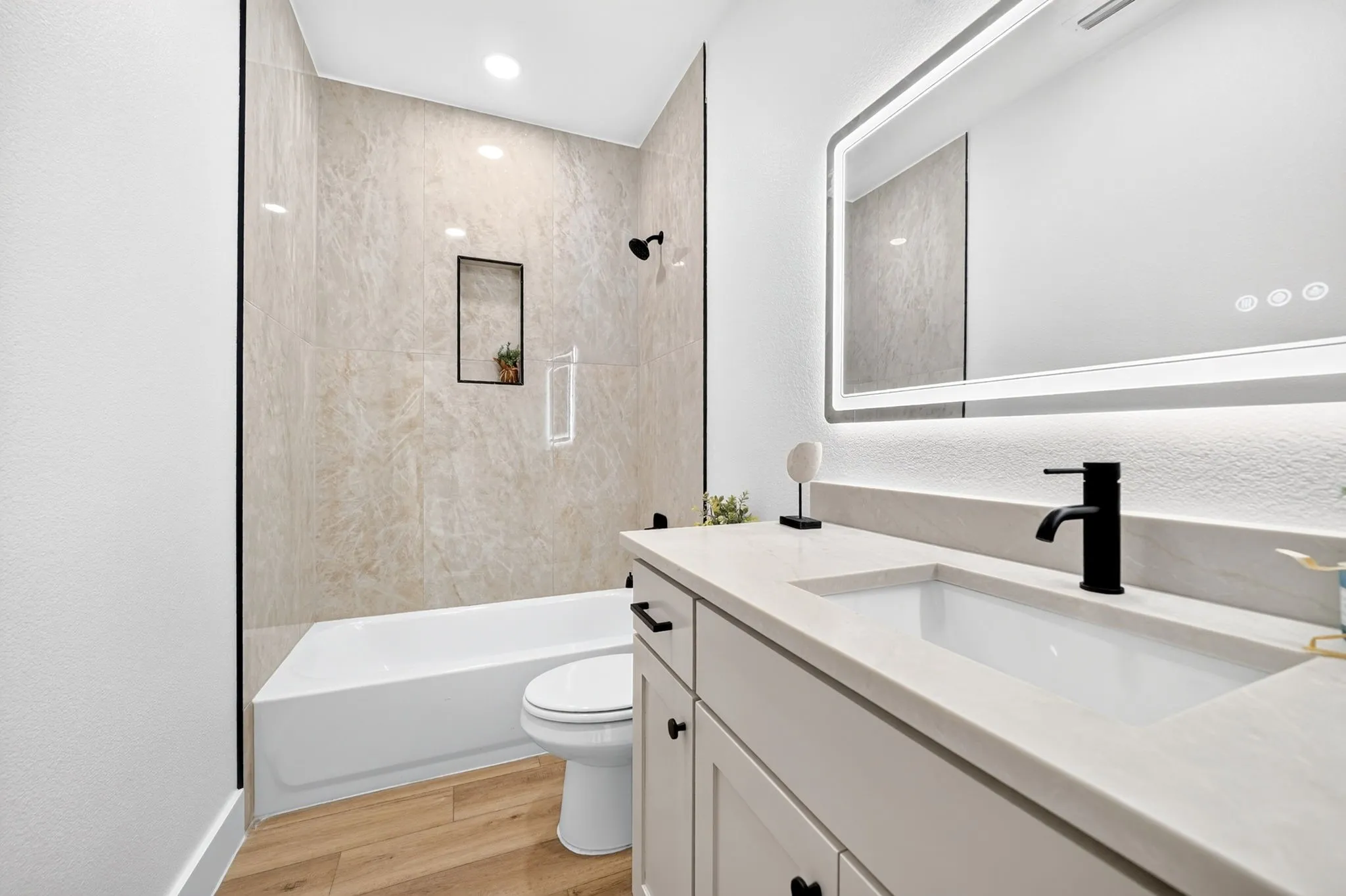 Bathtub and shower combination with floor-to-ceiling tiled surround, integrated shower niche, and matte black fixtures