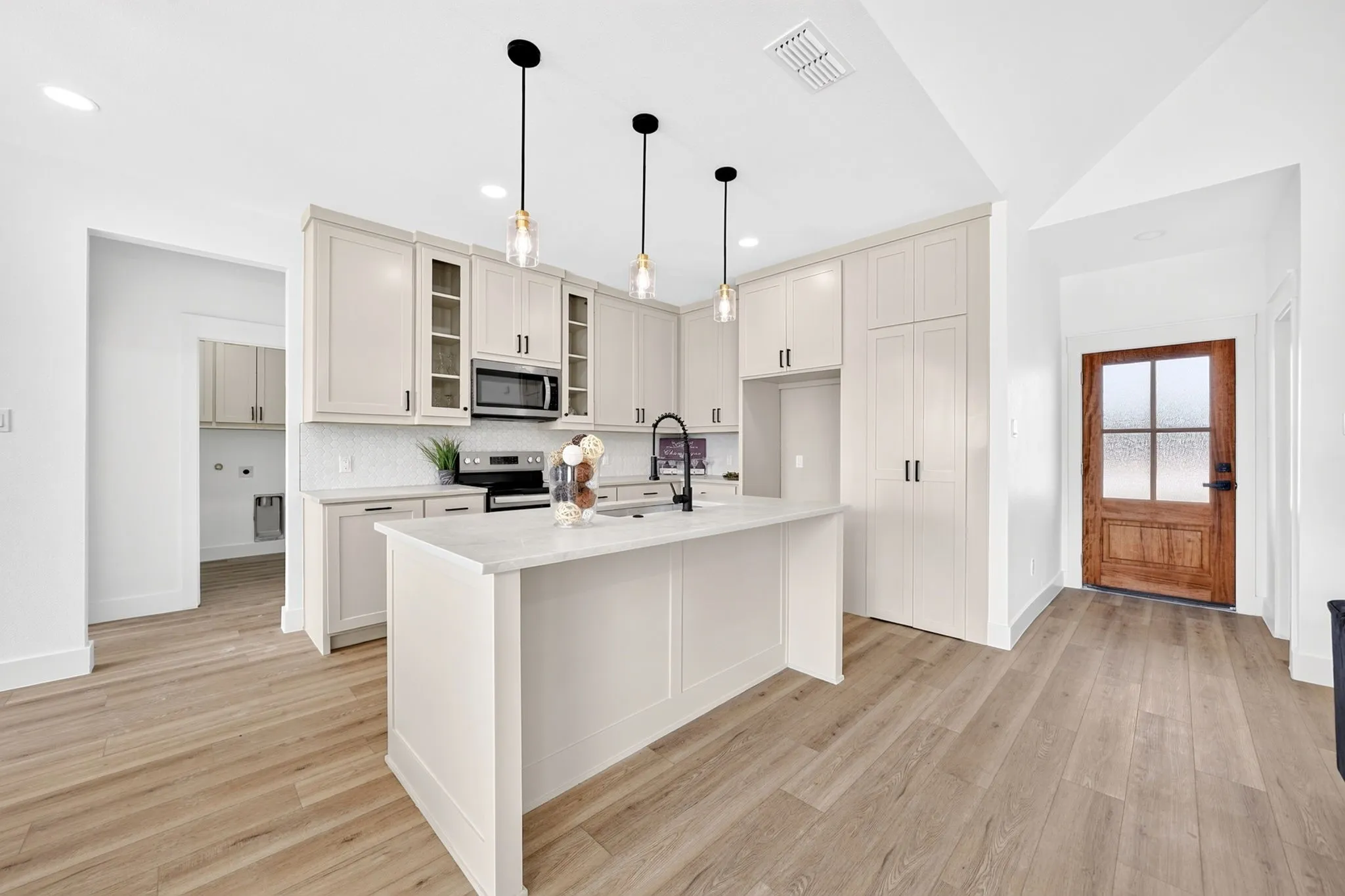 Kitchen featuring light-toned cabinetry, a central island with a countertop, wood-finish flooring, a stainless steel microwave, and pendant lighting