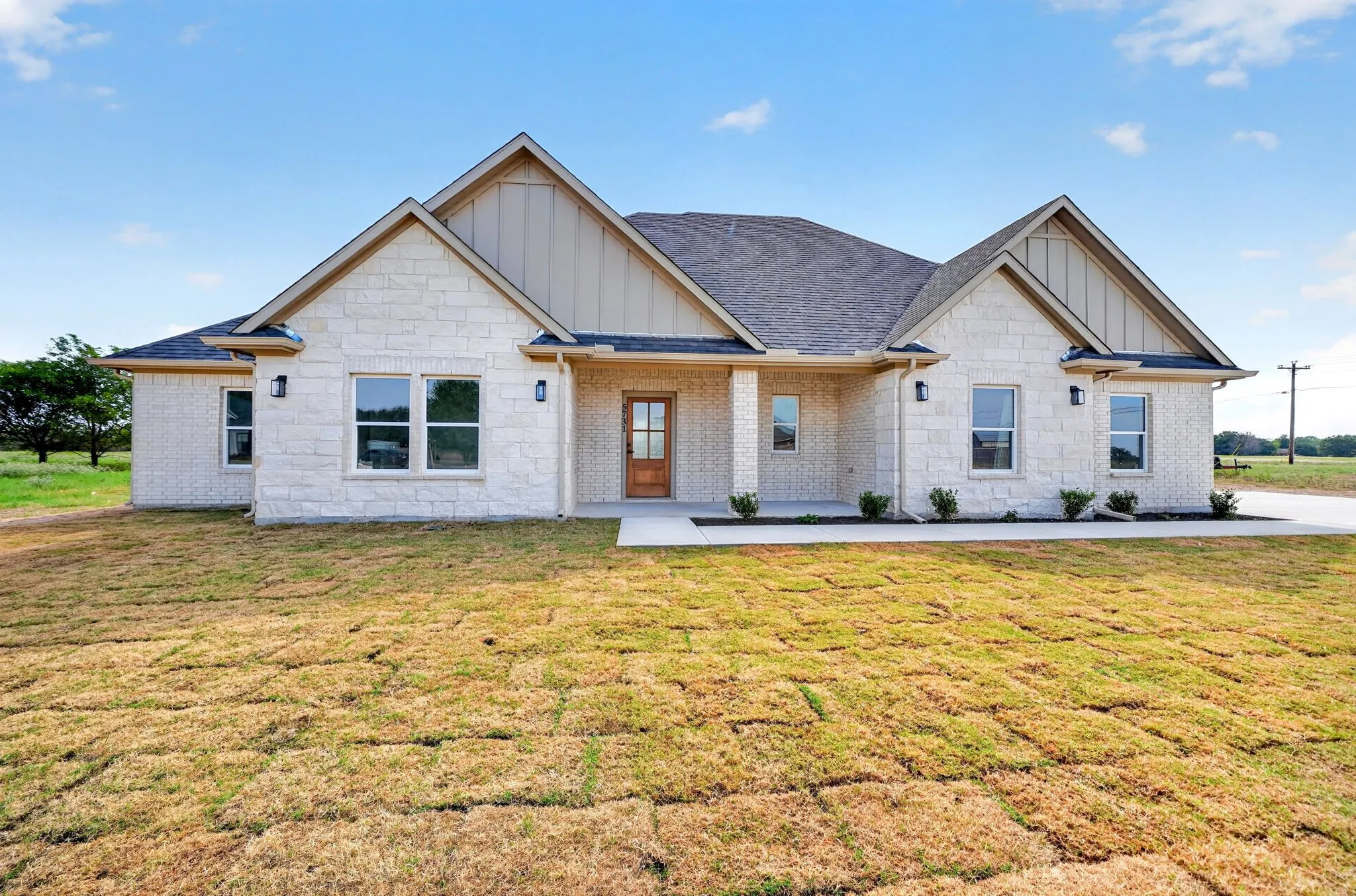 Stone veneer exterior, gable rooflines, covered entry, wood-finish front door, and multiple windows