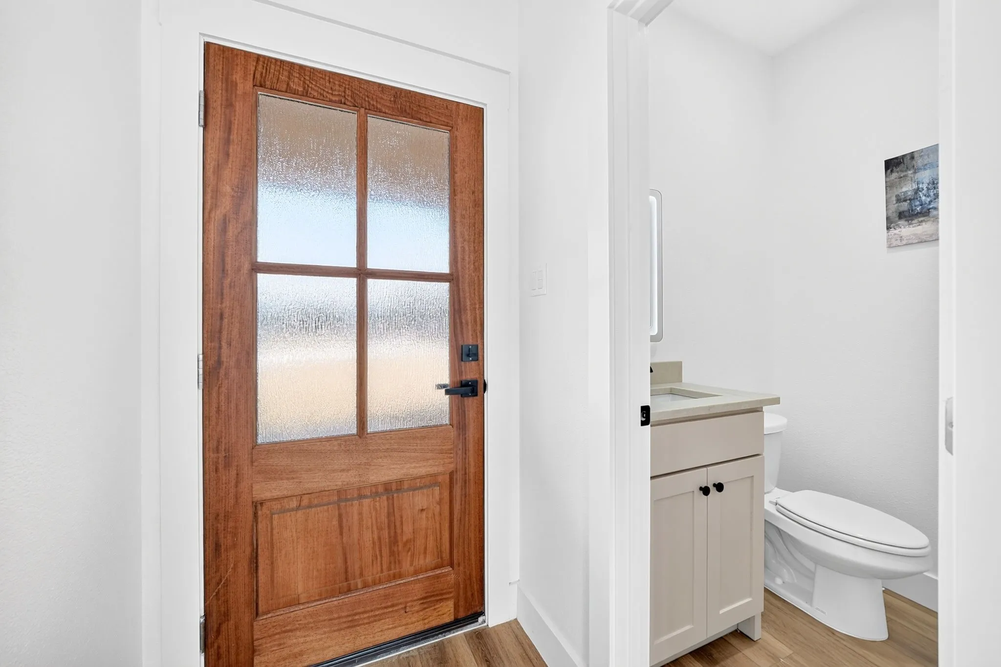 Wood-paneled door with frosted glass inserts, matte black hardware, wood-finish flooring, and a vanity with a light-colored countertop