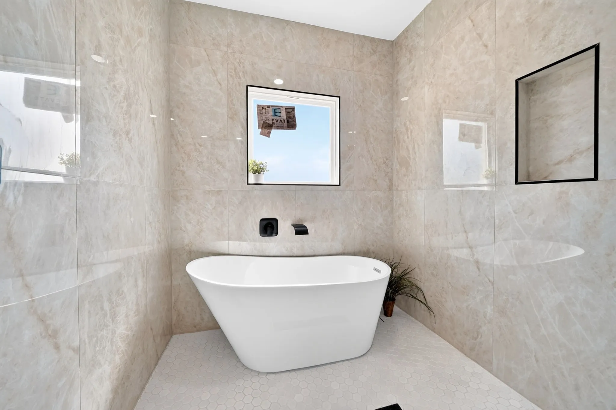 Freestanding soaking tub with wall-mounted matte black fixtures, set against full-height polished tile walls