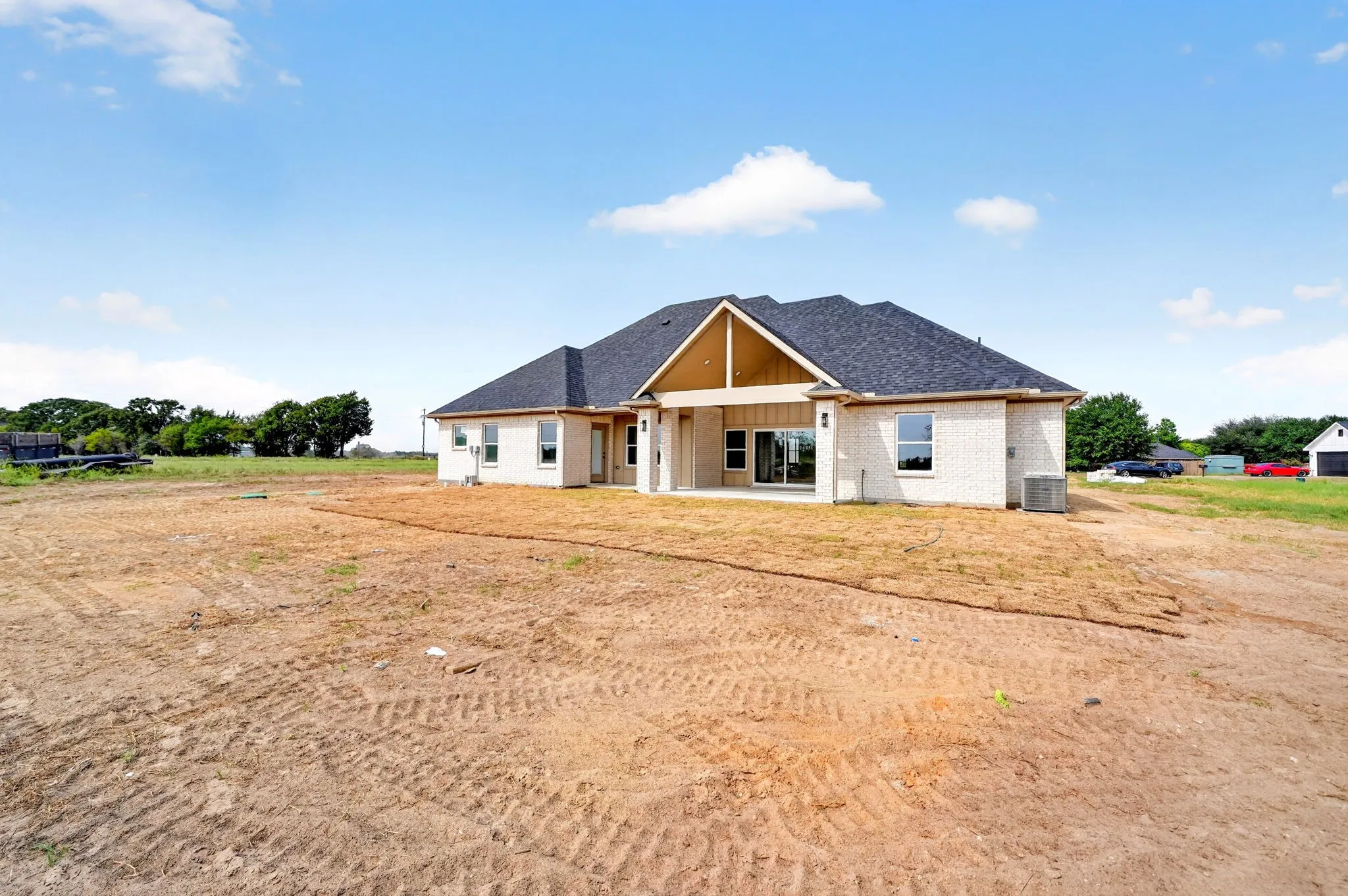 White brick exterior, dark shingle roof, covered patio, sliding glass doors, exposed wood-finish gables