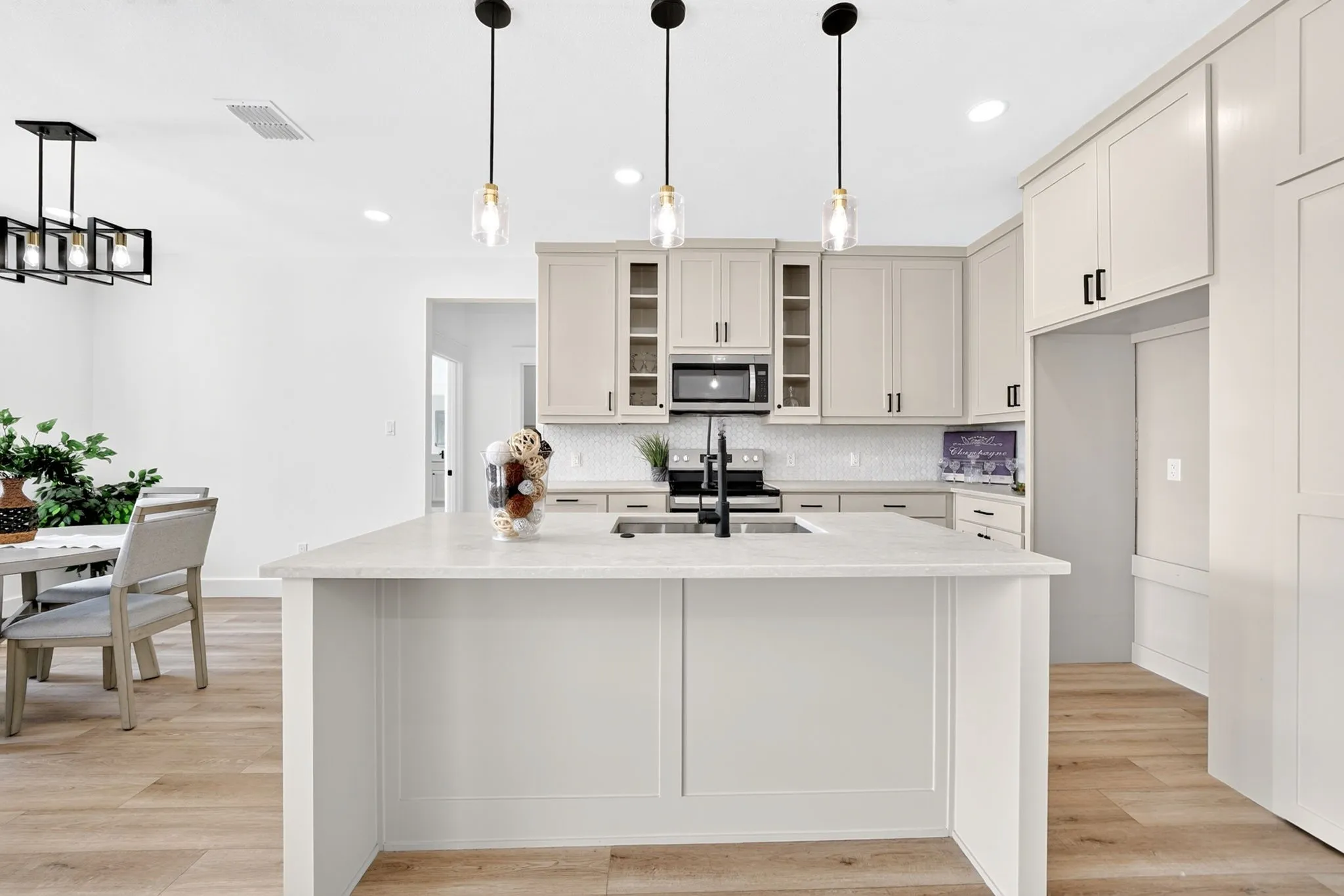 Kitchen island with a light-toned countertop, pendant lighting, built-in microwave, white subway tile backsplash, and light-toned cabinetry with dark hardware