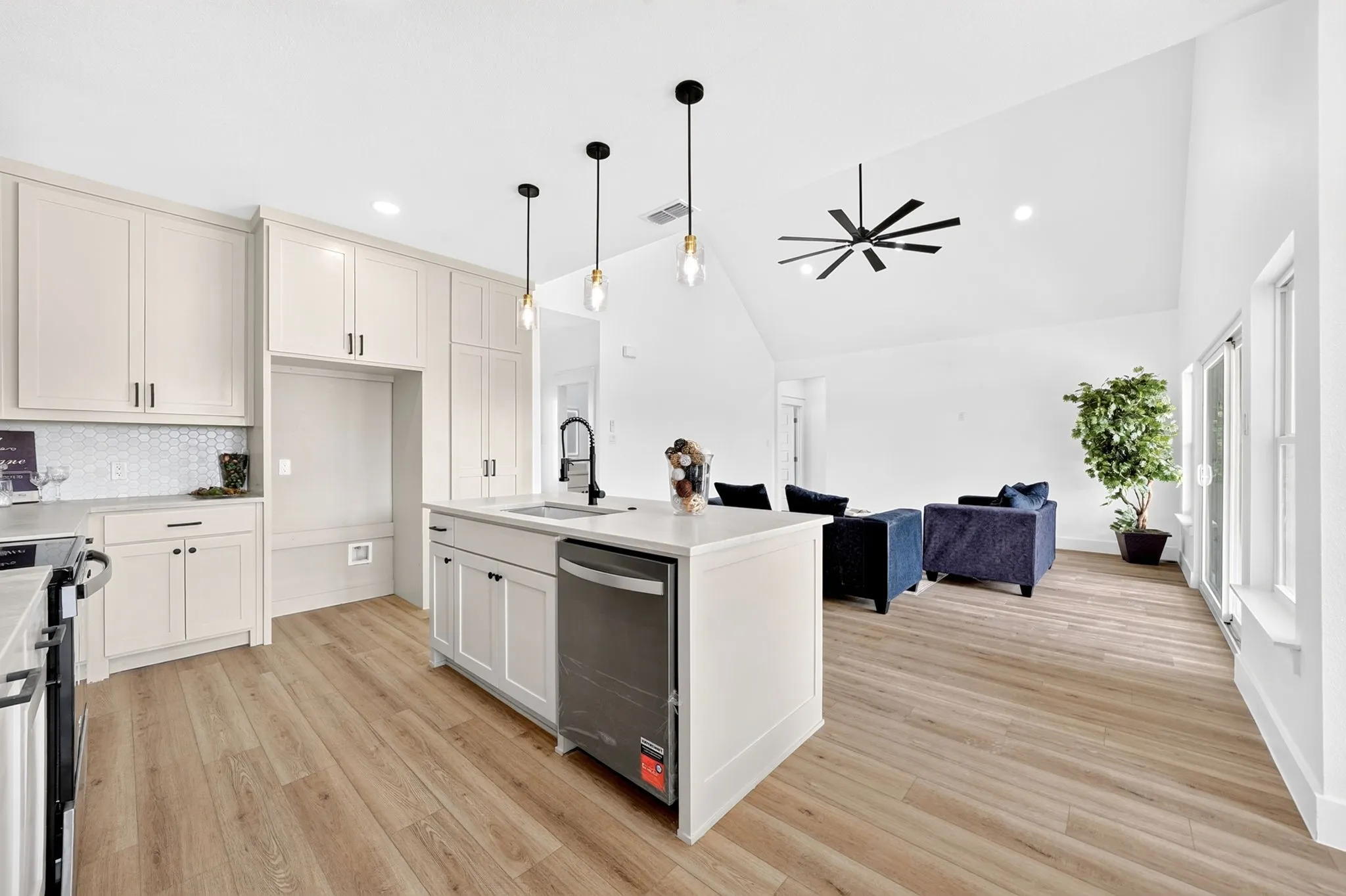 Kitchen island with a built-in sink and dishwasher, light wood-finish flooring, vaulted ceiling with a ceiling fan, and sliding glass doors