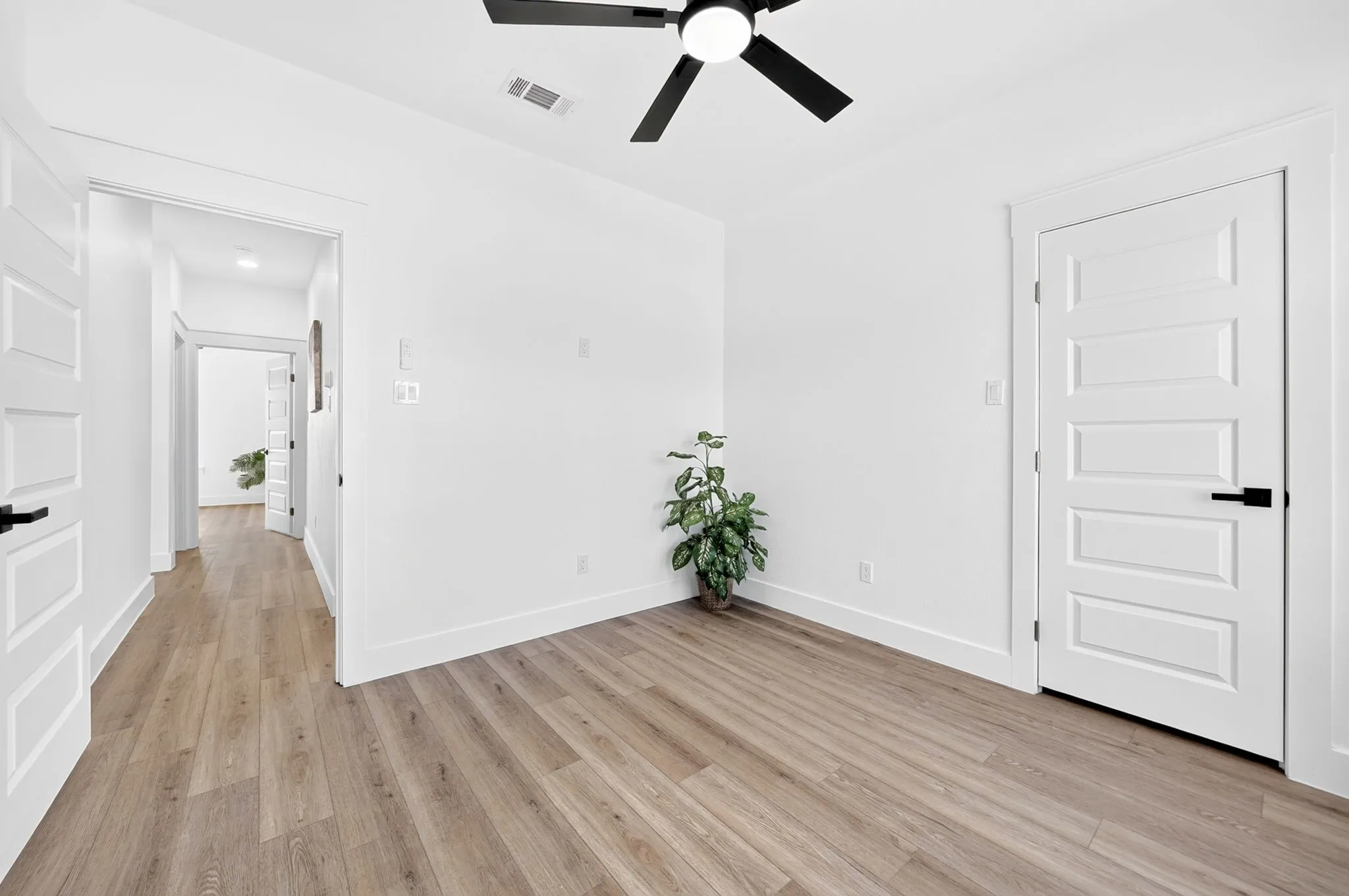 Wood-finish flooring, white walls, five-panel interior doors with black hardware, and a ceiling fan with integrated lighting