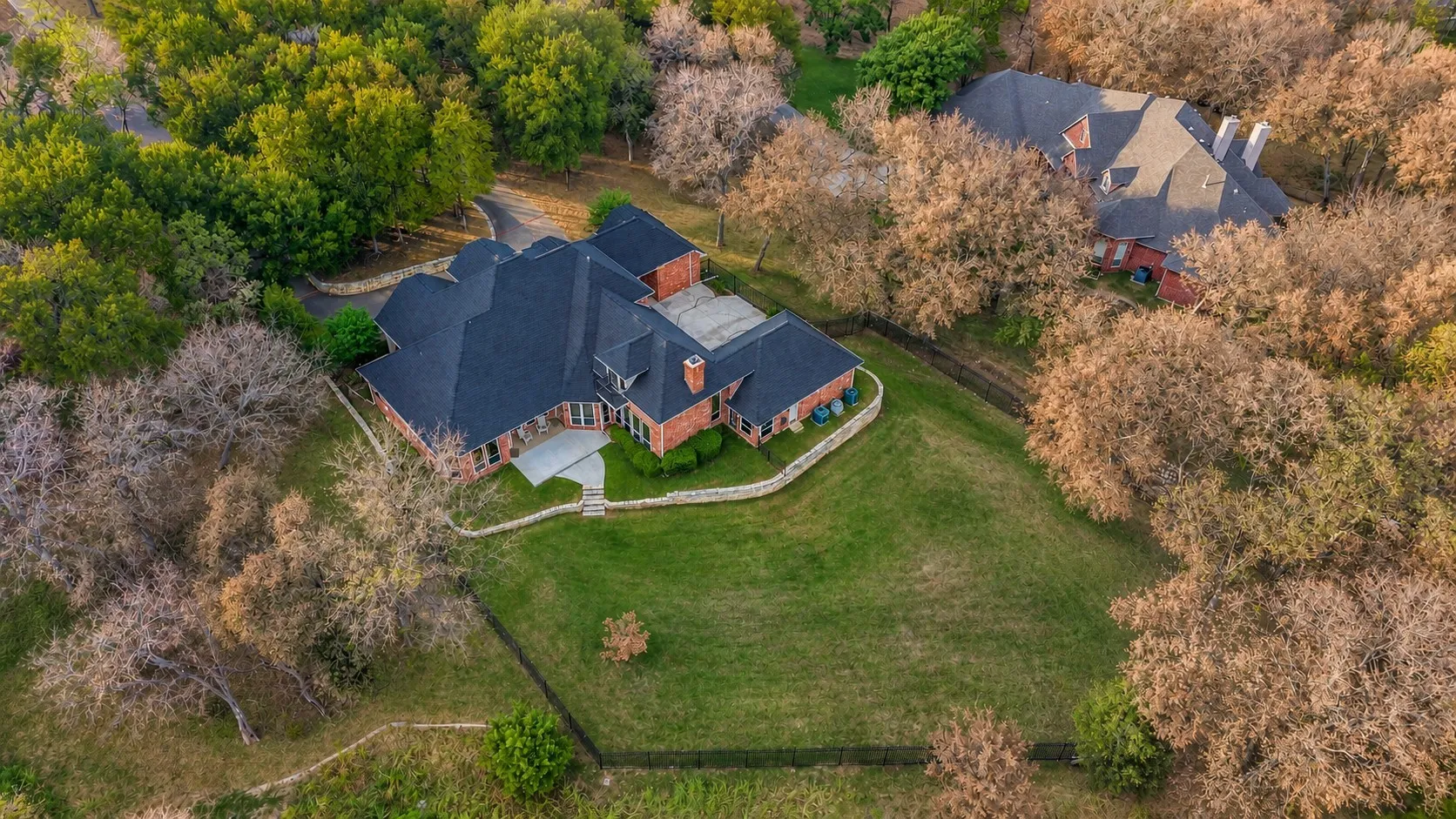 Sprawling brick estate surrounded by mature trees, expansive lawn, private fencing, and peaceful wooded scenery