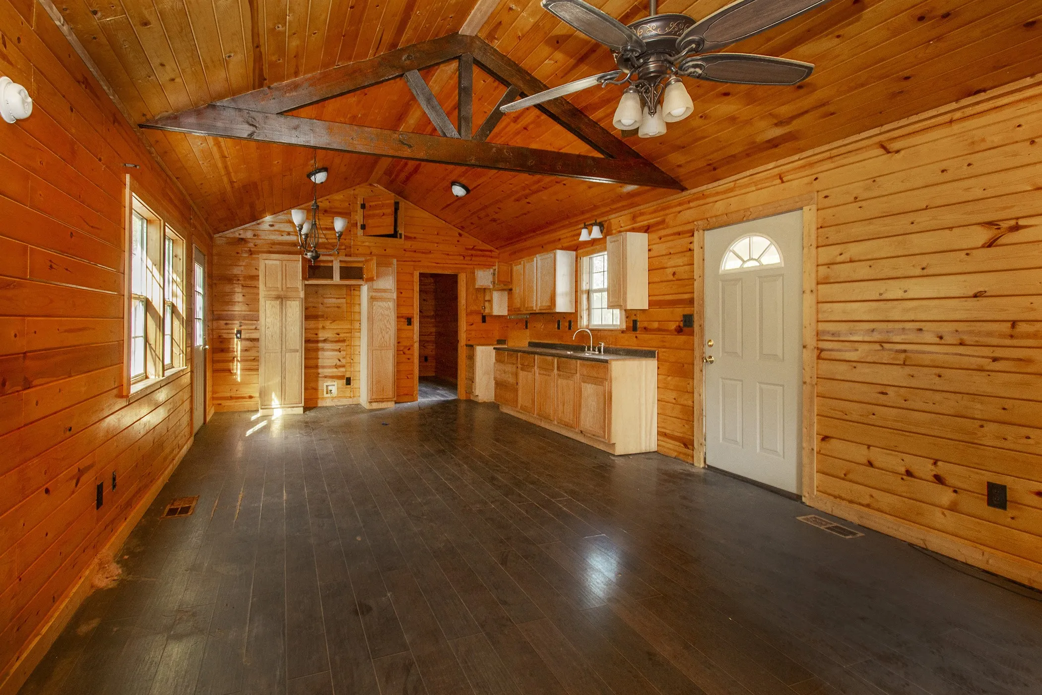 Vaulted wood-paneled ceiling with exposed beams, wood-finish flooring, wood-paneled walls, built-in cabinetry, and ceiling fan with integrated lighting