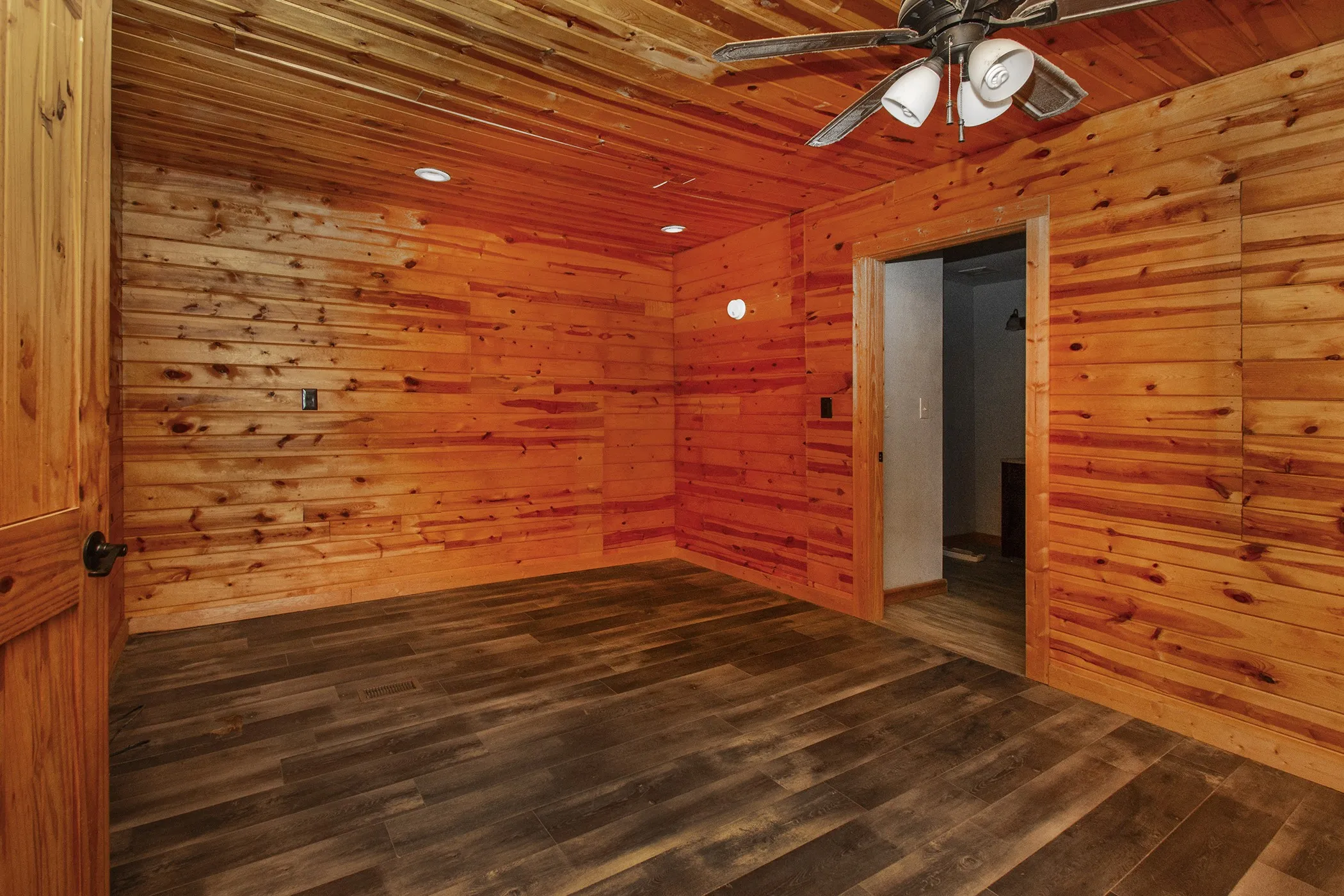 Wood-finish flooring, wood-paneled walls, wood-paneled ceiling, recessed lighting, and a ceiling fan with integrated lighting