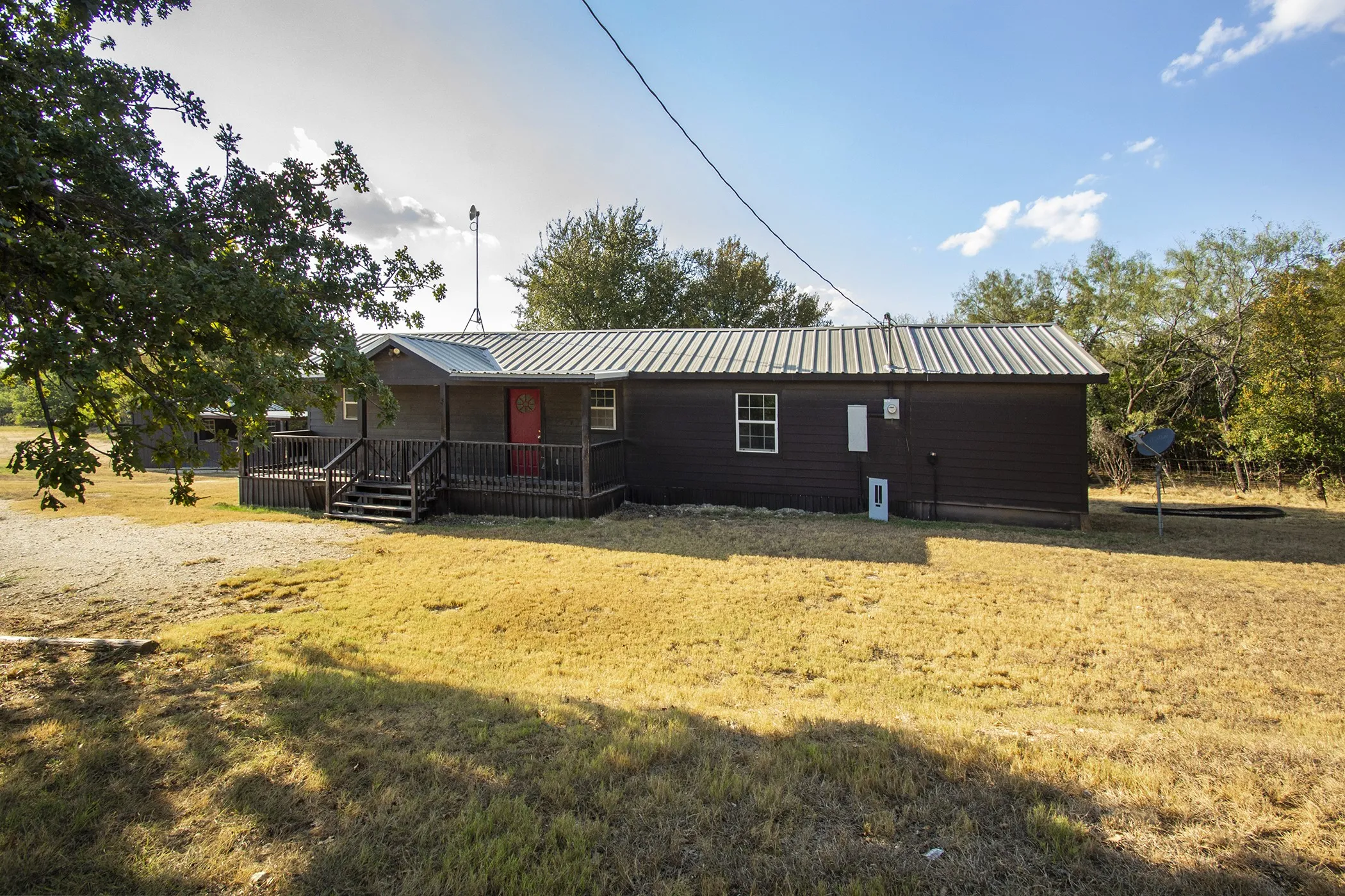 Exterior featuring dark siding, a covered porch with railings, a red entry door, and a corrugated metal roof