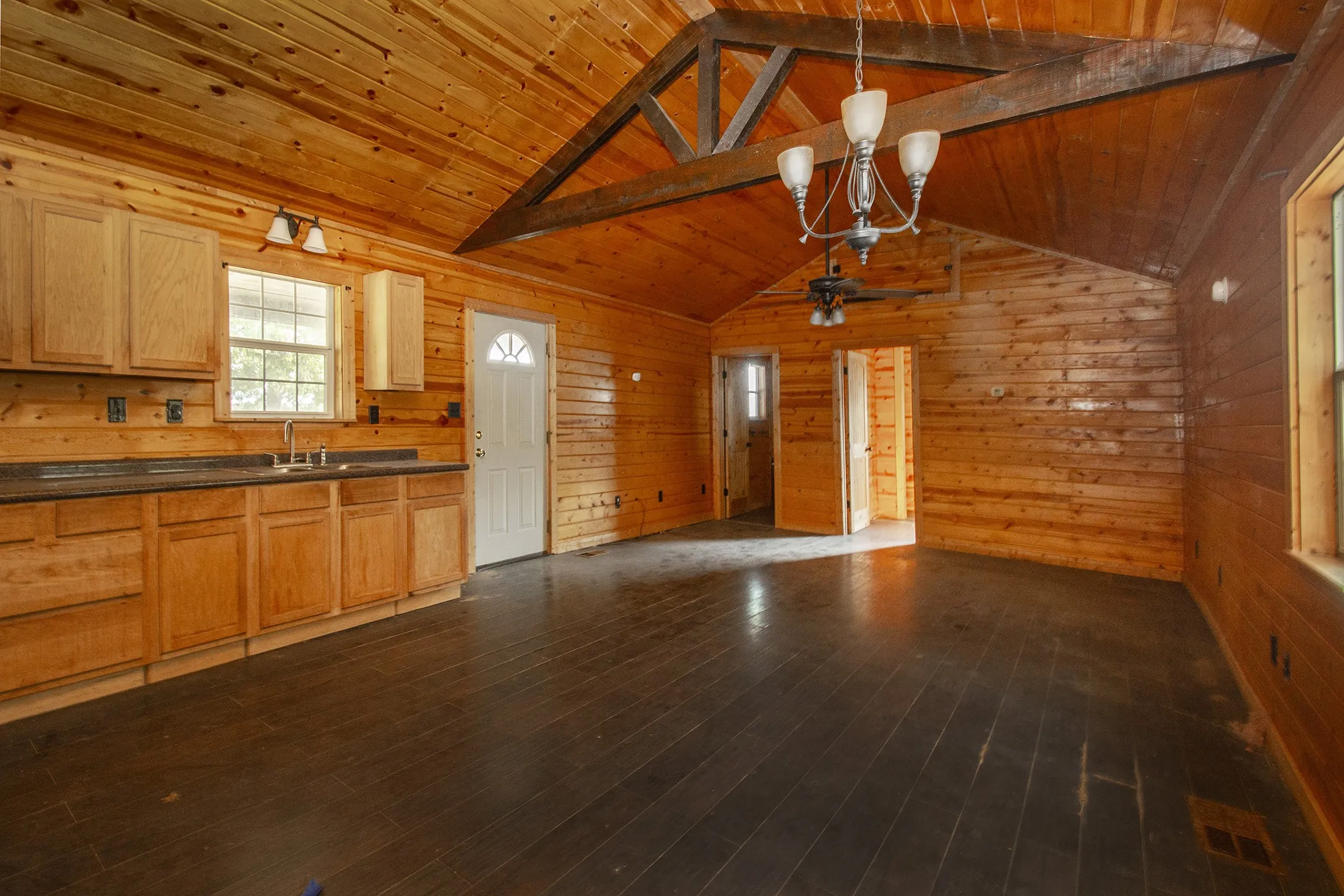Vaulted wood-paneled ceiling with exposed wood beams, wood-finish flooring, wood cabinetry with dark countertops, and a ceiling fan with light fixture
