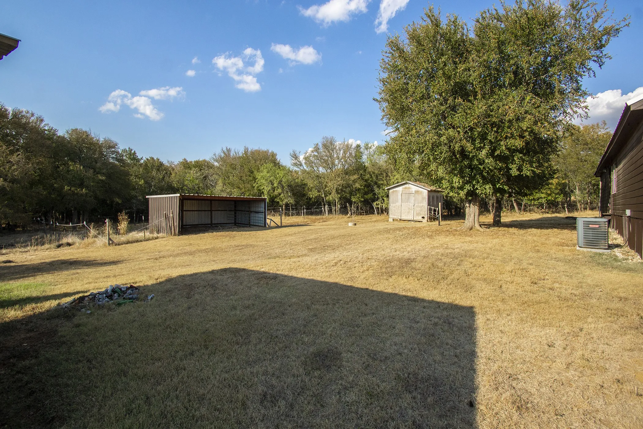 Expansive outdoor space featuring a large open-sided shed, a detached smaller shed, and mature trees