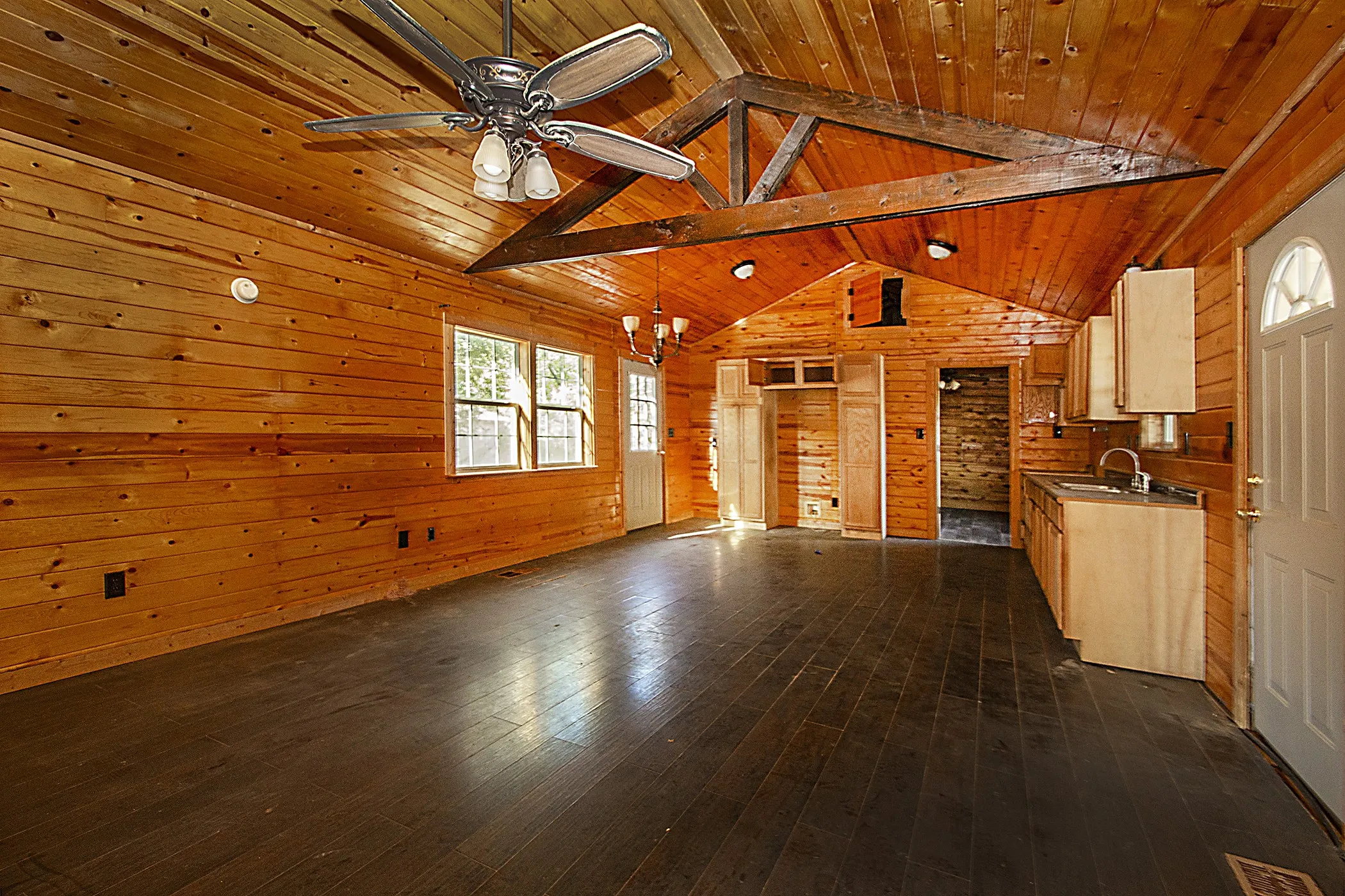 Vaulted ceiling with exposed wood beams, wood-plank walls, dark wood-finish flooring, and built-in wood cabinetry