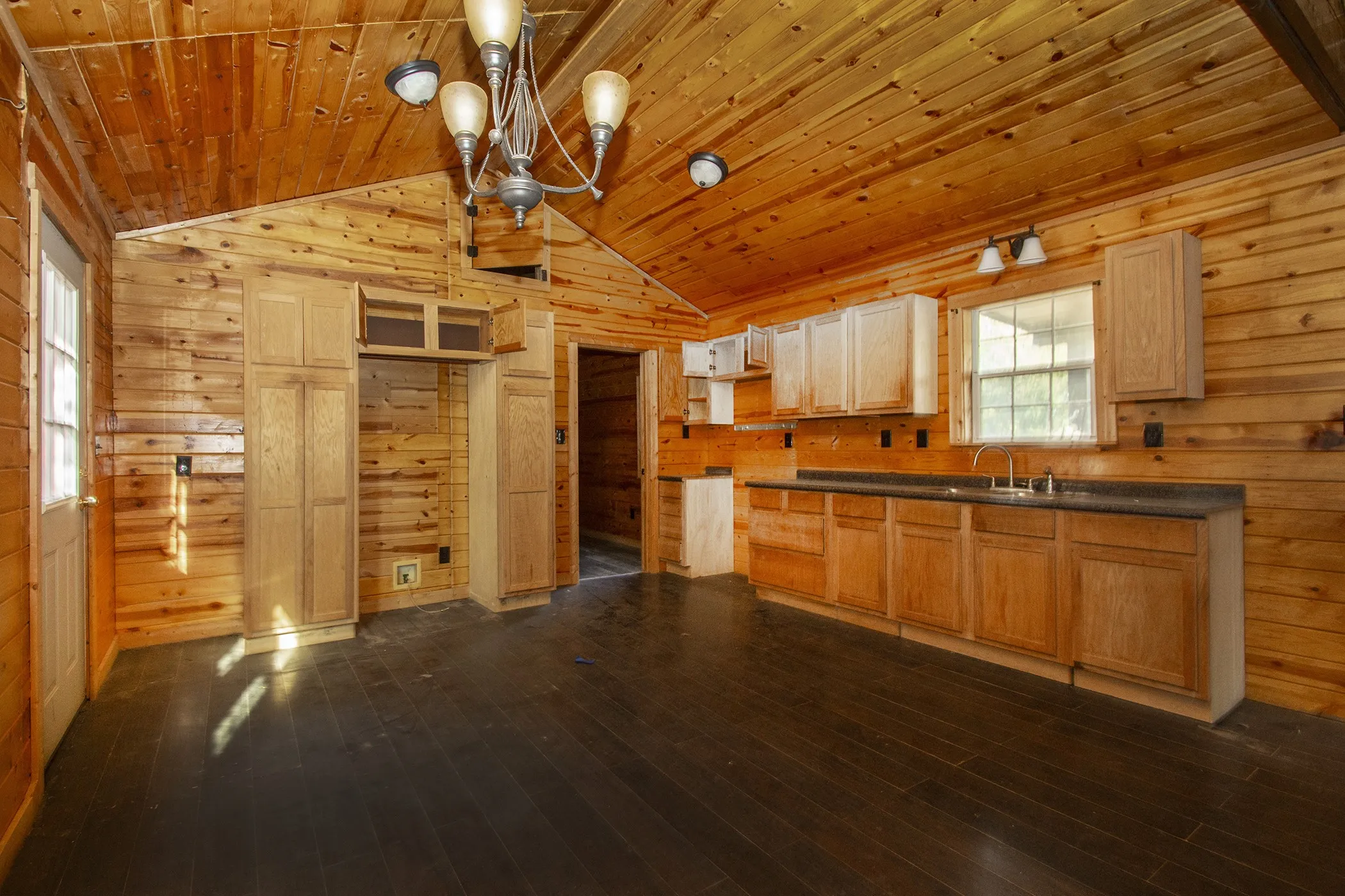 Vaulted wood-paneled ceiling, wood-finish walls, dark wood-finish flooring, light wood cabinetry, and built-in stainless steel sink