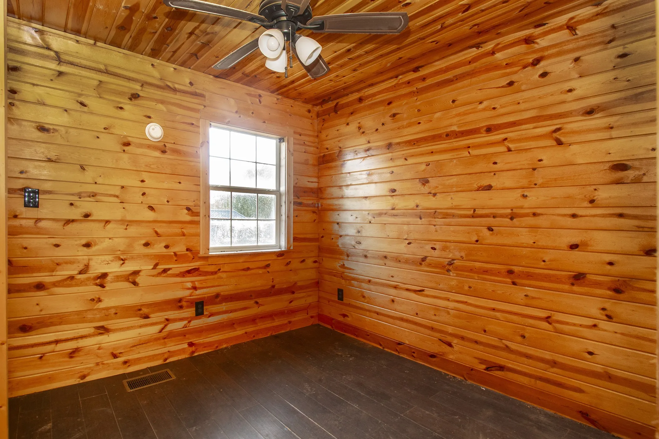 Wood-paneled walls and ceiling, dark wood-finish flooring, and a ceiling fan with integrated lighting