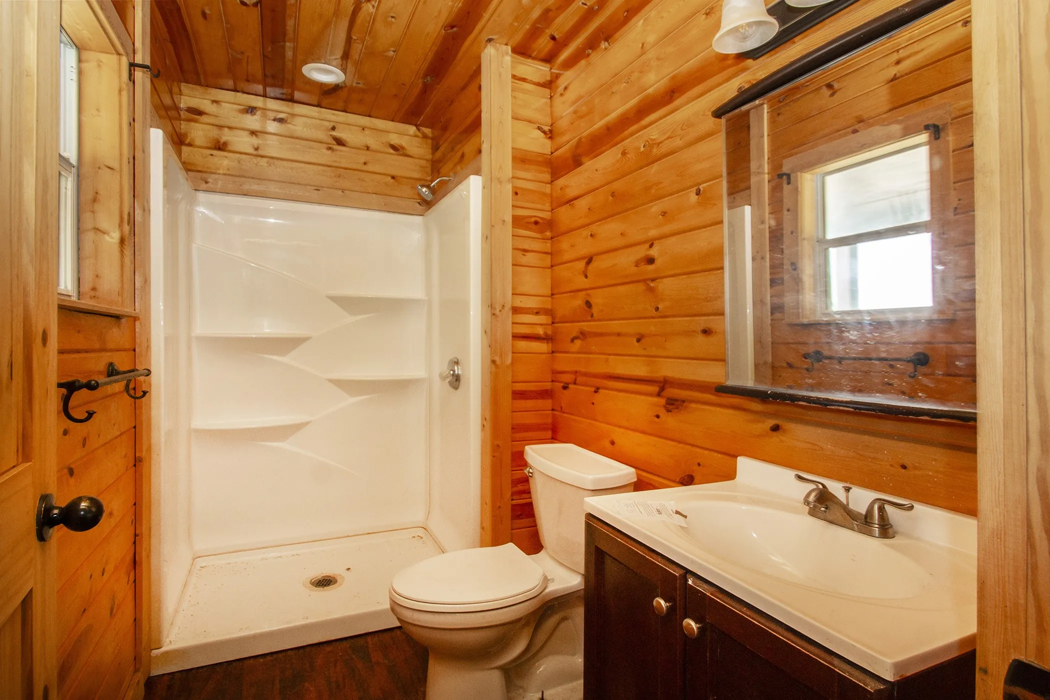 Wood-paneled walls and ceiling, full shower with built-in shelving, dark wood-finish vanity with integrated sink, and wall-mounted mirror