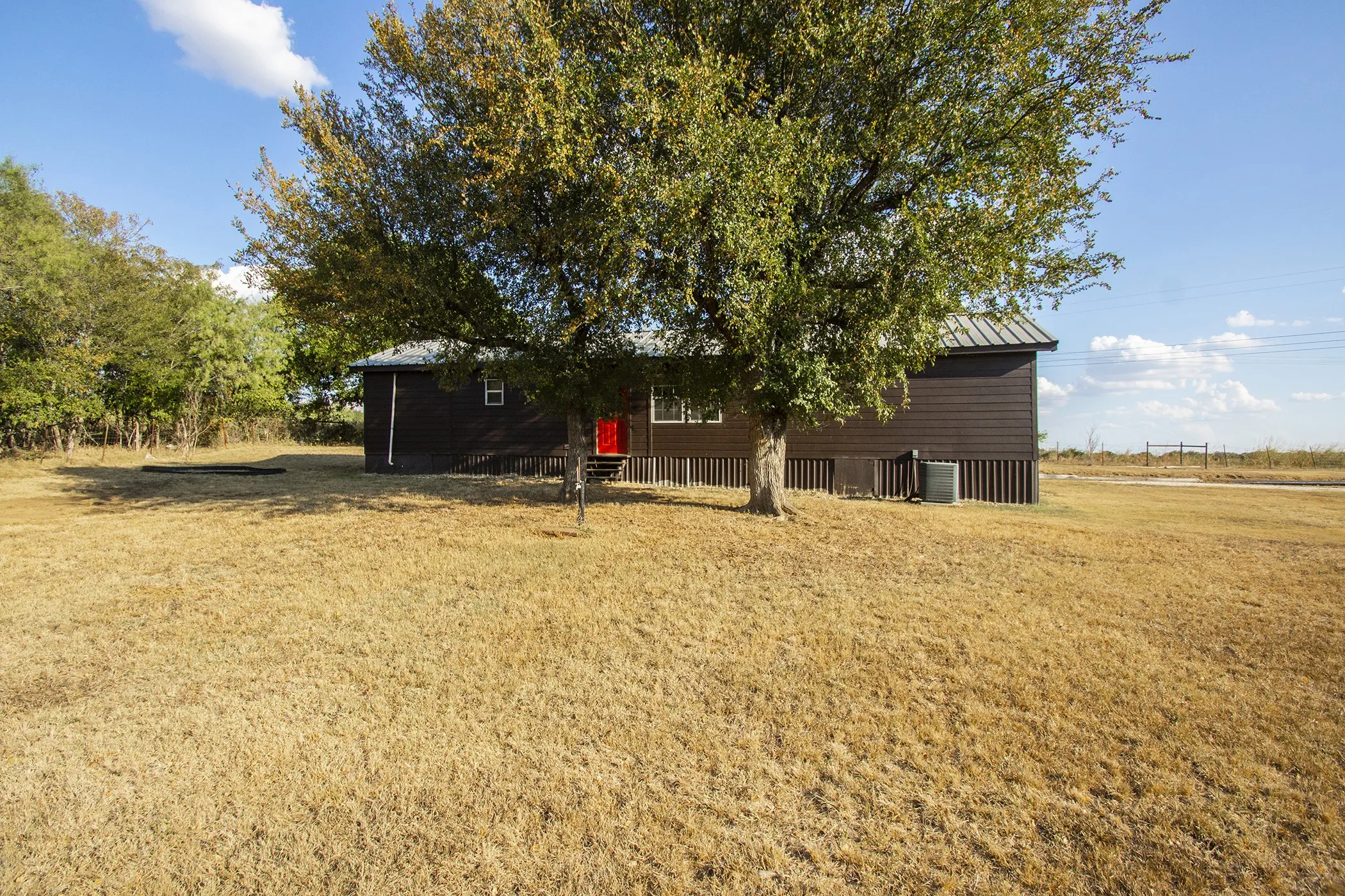 Expansive property featuring a brown horizontal siding exterior, a red entry door, and a mature tree