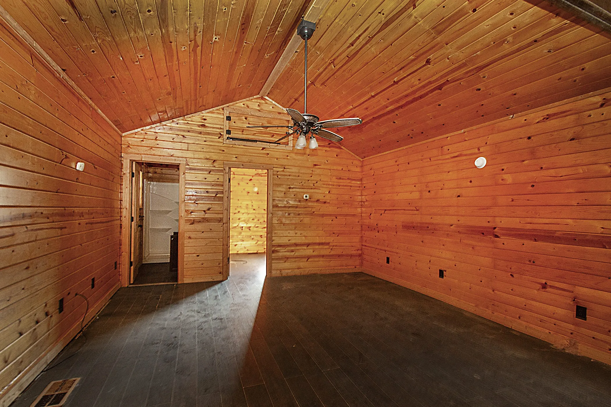 Vaulted wood-paneled ceiling, wood-paneled walls, wood-finish flooring, ceiling fan with integrated lighting, and interior doorway