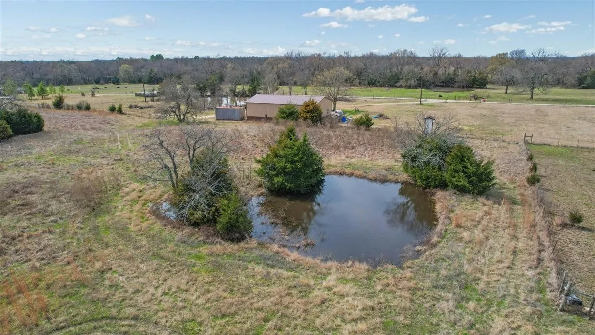Expansive acreage featuring a natural pond, mature trees, and a distant building with a metal roof