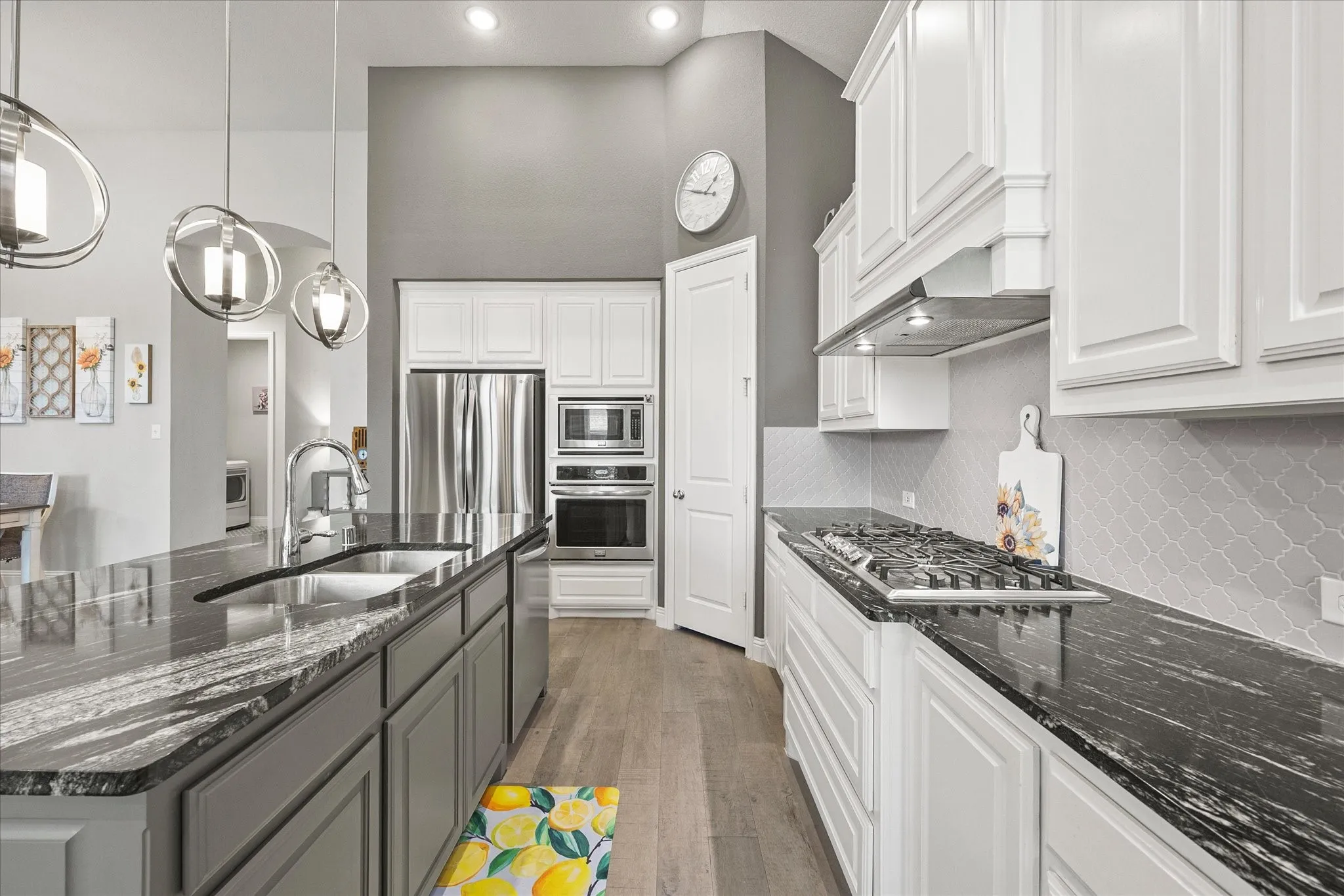 Kitchen featuring an expansive island with an undermount sink, stainless steel appliances, white cabinetry, wood-finish flooring, and a patterned tile backsplash