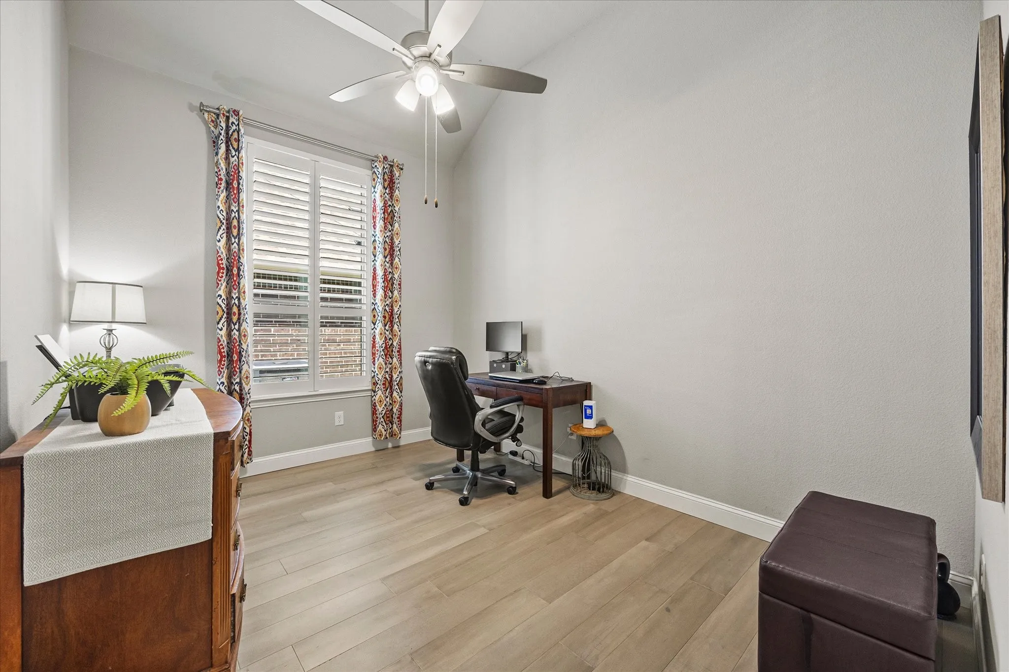Vaulted ceiling with ceiling fan, wood-finish flooring, window with plantation shutters, and recessed wall panel