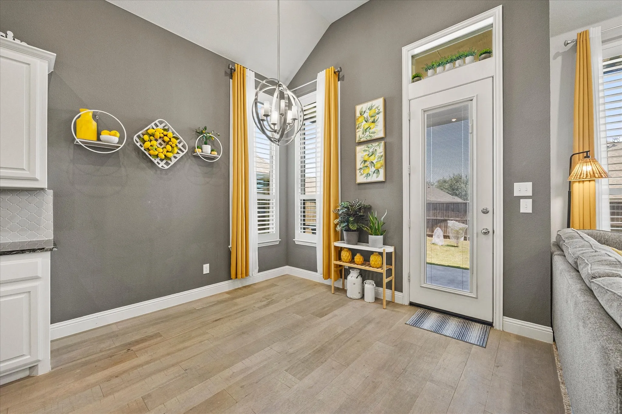 Vaulted ceiling, wood-finish flooring, white cabinetry, gray wall color, and a full-light exterior door