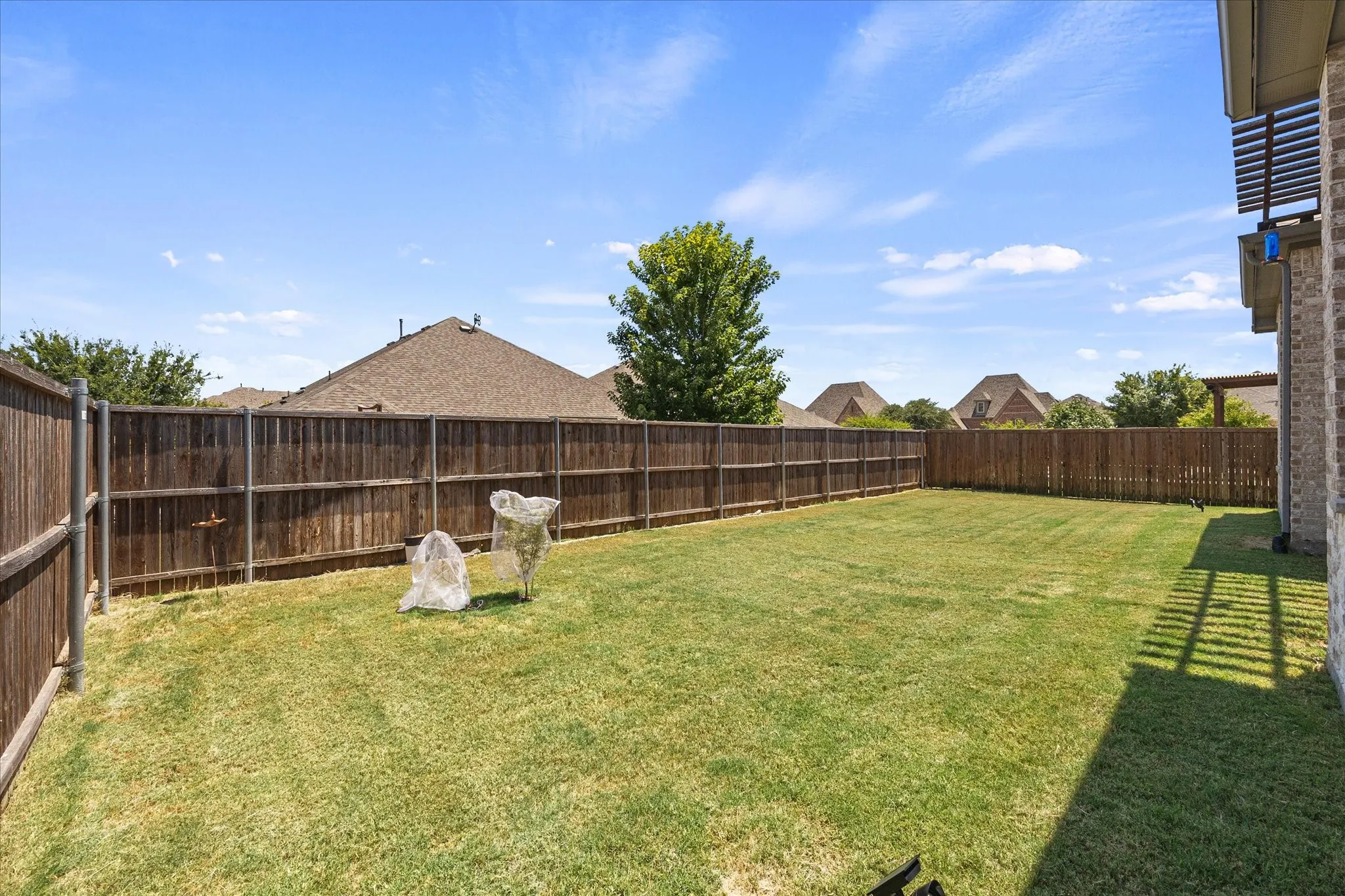 Expansive backyard featuring a manicured lawn, full privacy fencing, and a brick exterior with a wood pergola