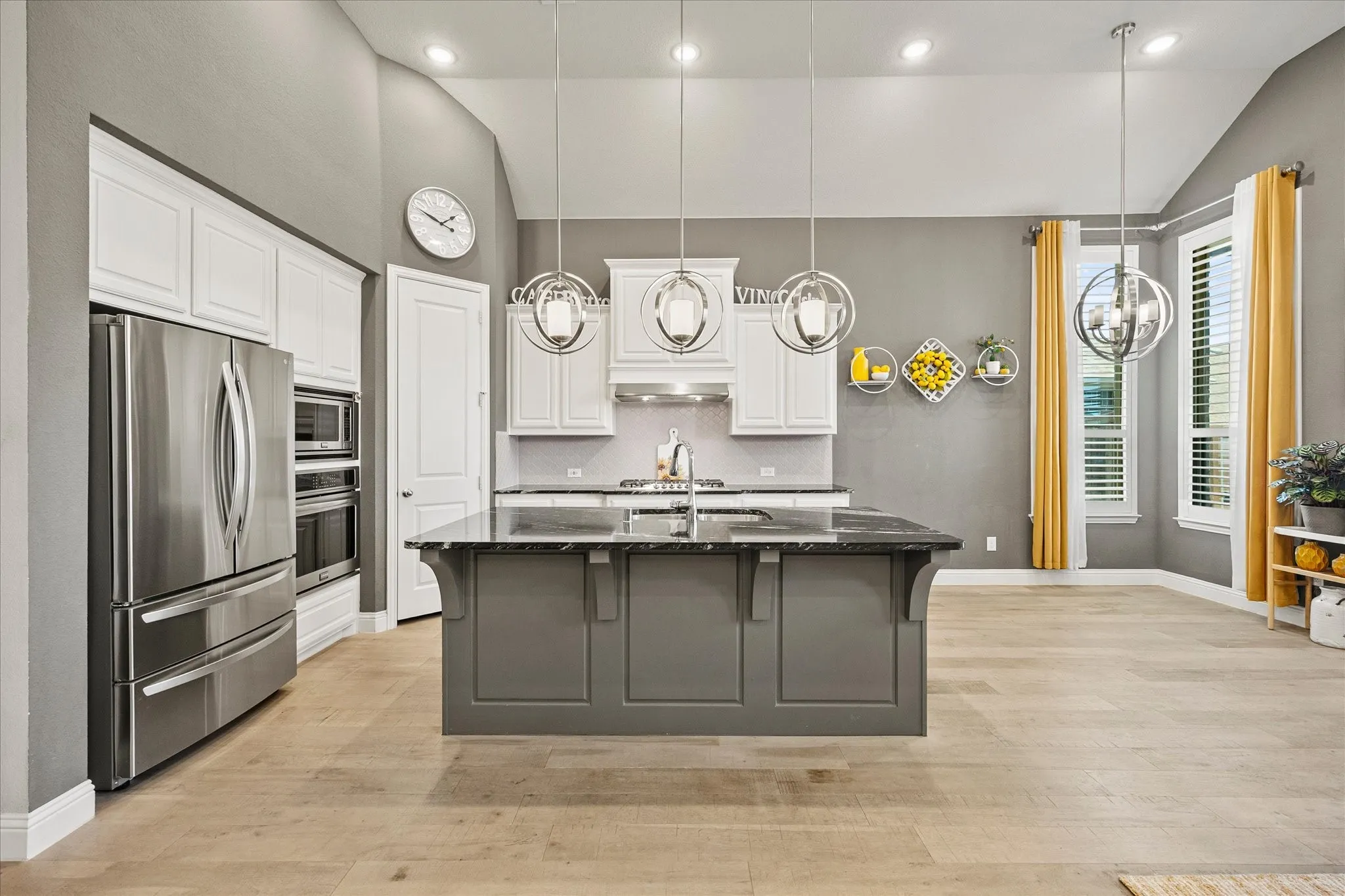 Kitchen featuring vaulted ceilings, stainless steel appliances, a center island with a dark countertop, white shaker cabinetry, and wood-finish flooring