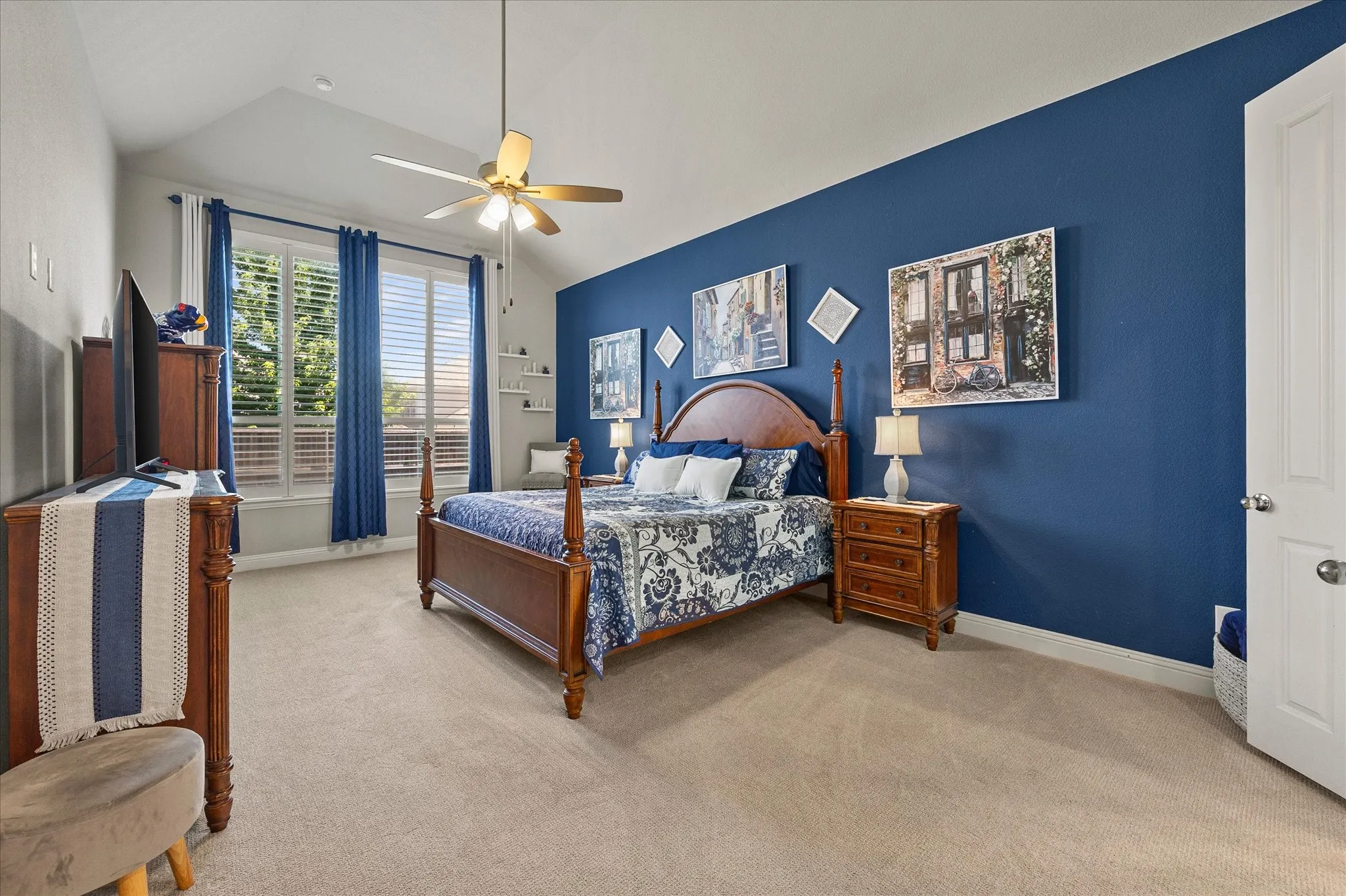 Vaulted ceiling with a ceiling fan, broad windows with horizontal blinds, rich blue accent wall, and neutral carpet flooring