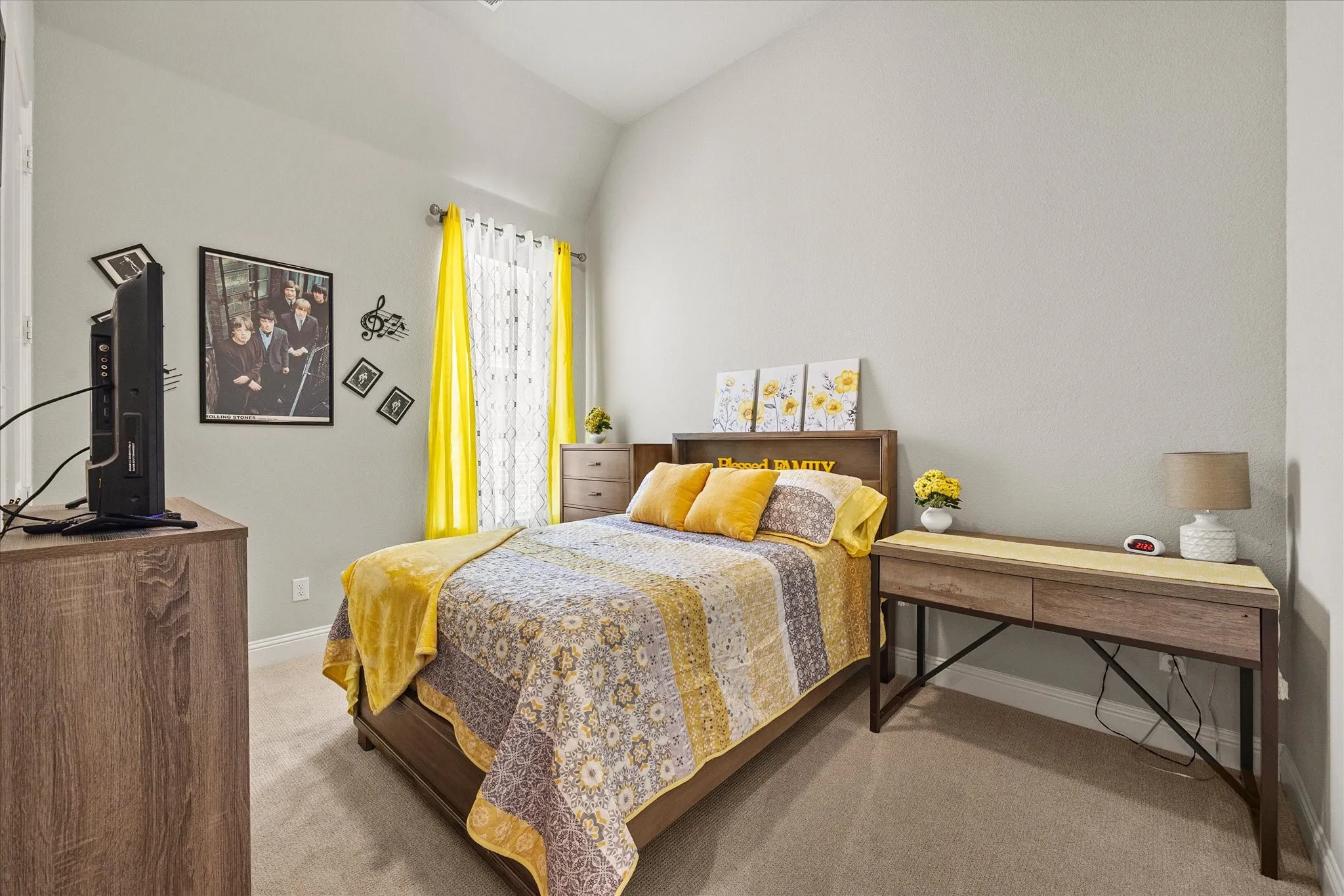 Vaulted ceiling, neutral wall paint, carpet flooring, window with sheer and solid curtains, wood-finish furniture