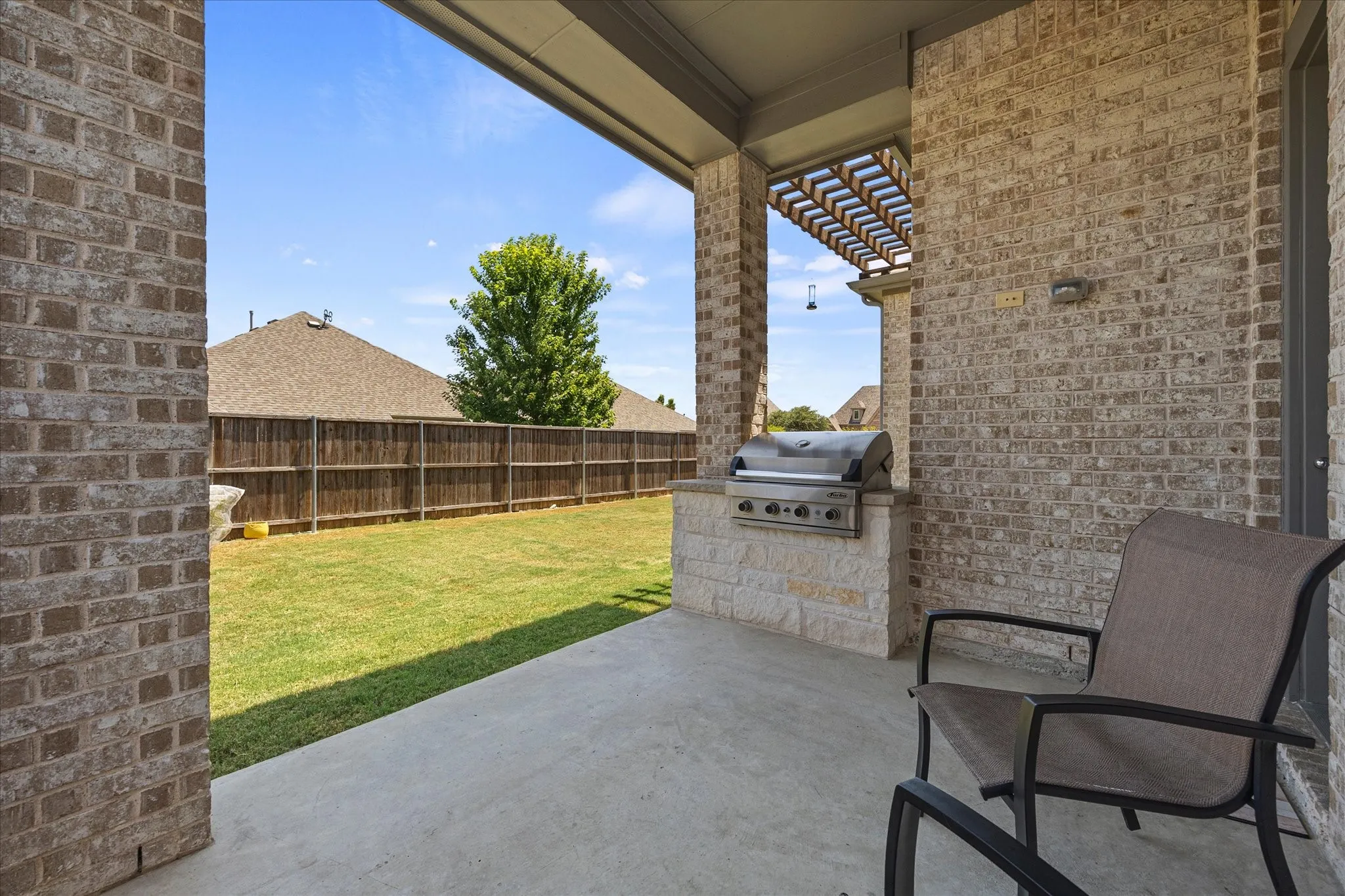 Covered patio with a built-in outdoor grill, a stone-faced base, and a wood pergola